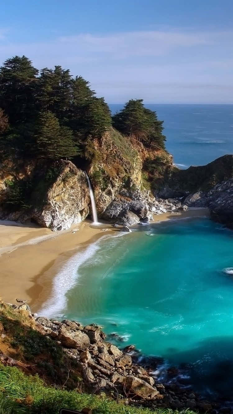 桌布 壁紙 — 一個迷人的海岸小灣，擁有碧綠的海水、沙灘和從懸崖傾瀉入海的瀑布，在清澈的藍天下。