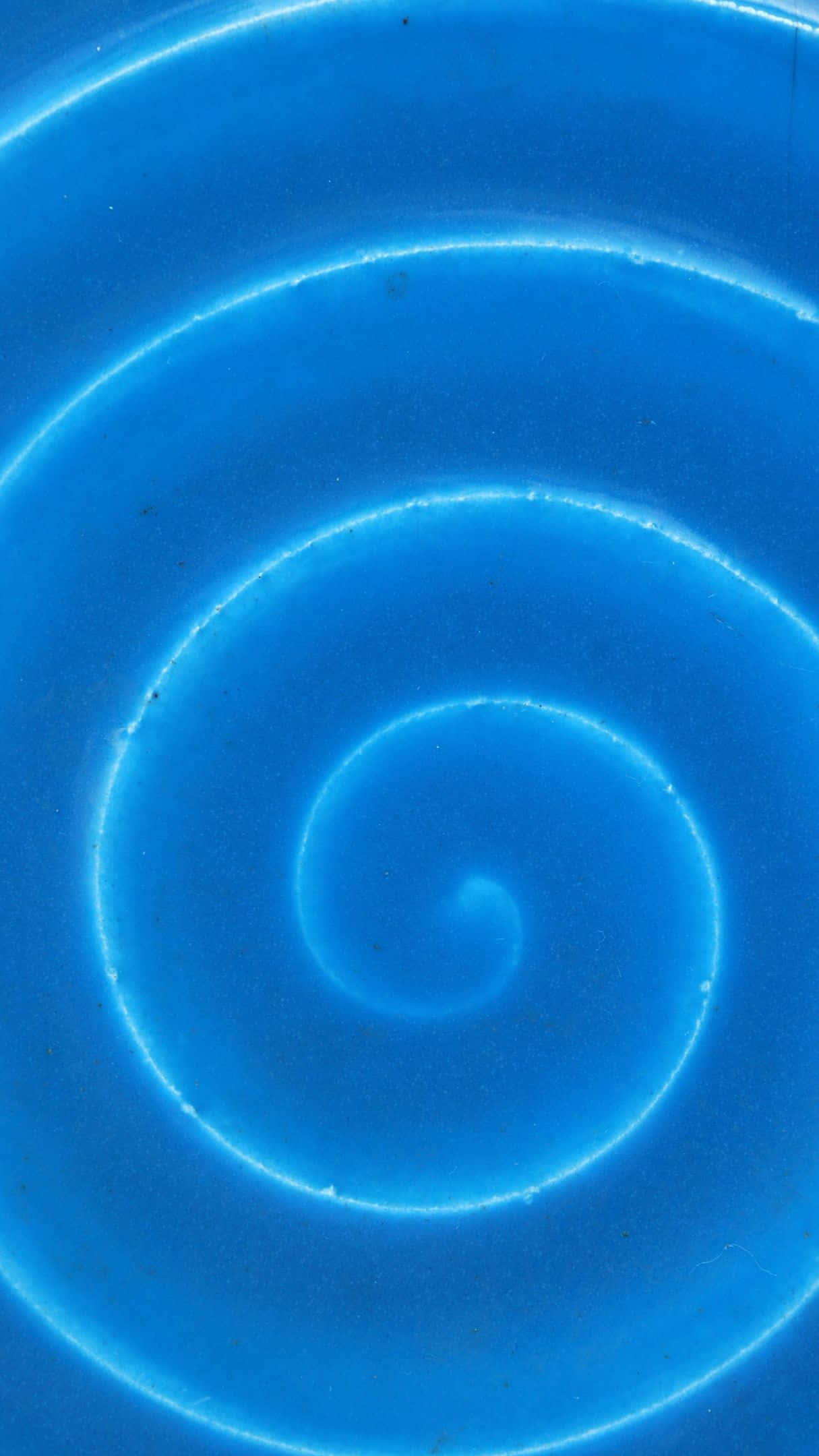 Blue Swirl 桌布 壁紙 — 一個迷人的螺旋圖案，以不同深淺的藍色呈現，在帶有紋理的陶瓷表面上散發柔和發光的邊緣。