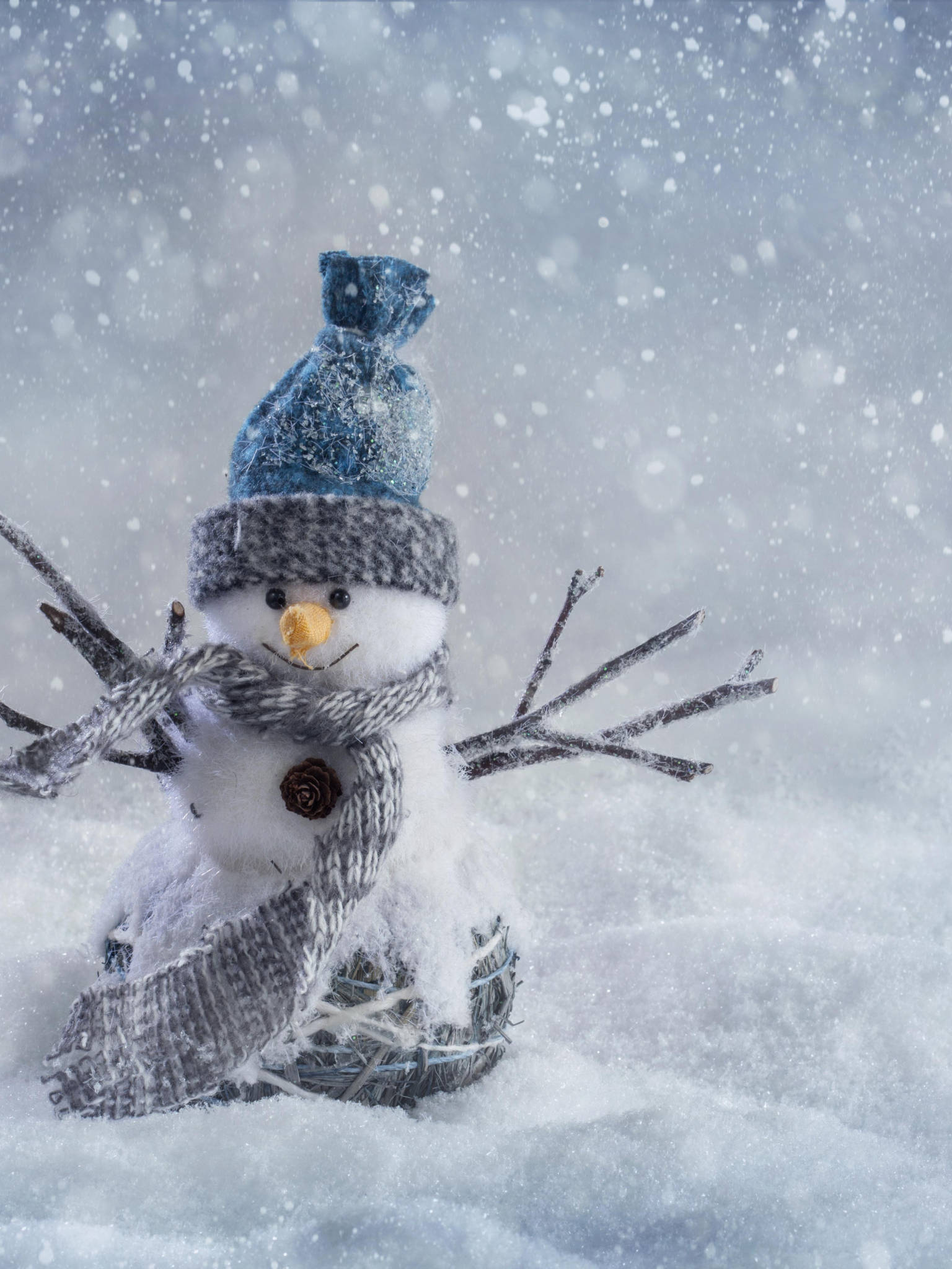 冬季 iPhone 壁紙 桌布 壁紙 — 一個迷人的雪人，戴著藍色帽子和灰色圍巾，站在雪景中，雪花輕輕飄落。