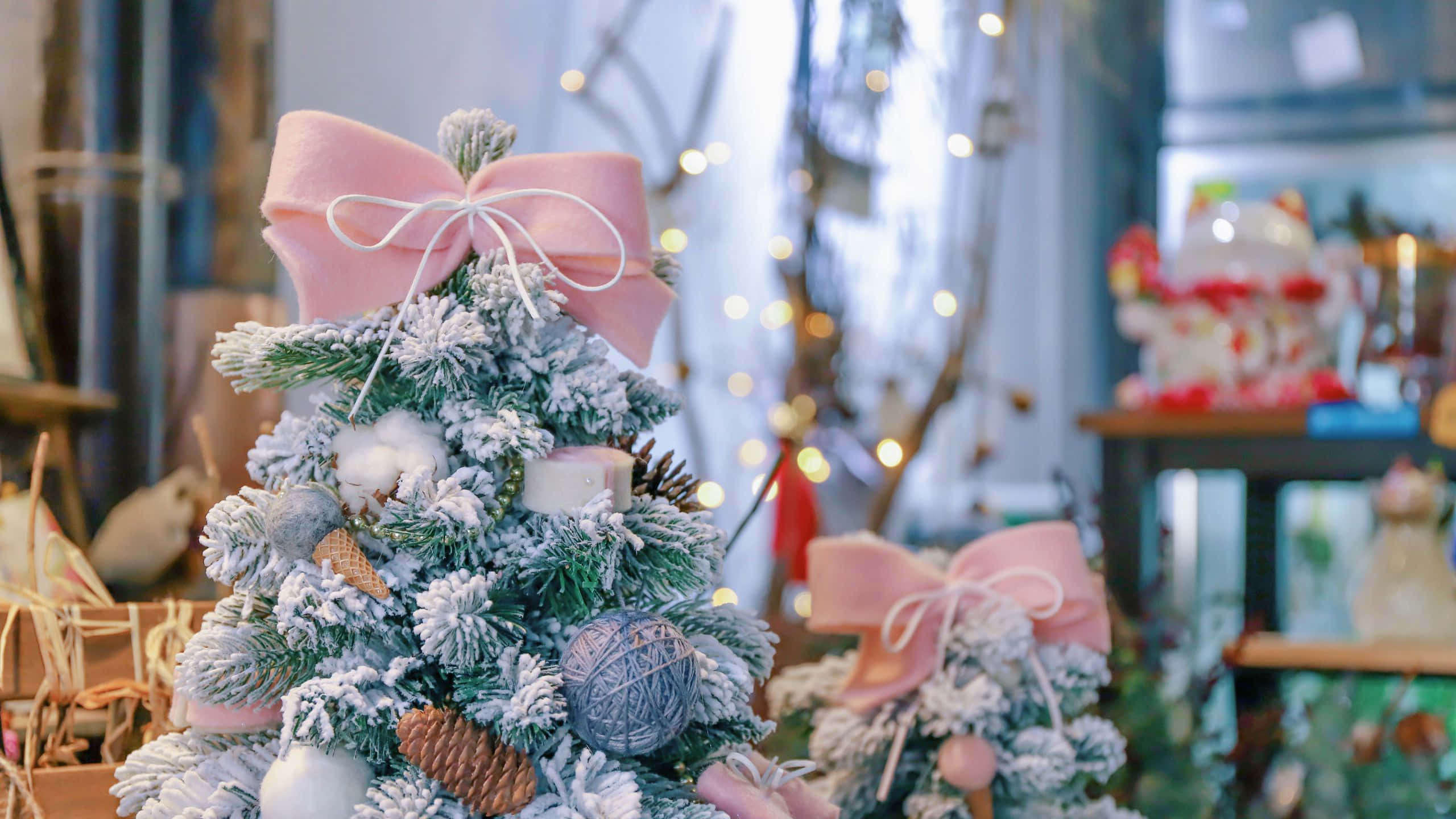 1920x1080 HD Christmas 桌布 壁紙 — 一個迷你霜凍聖誕樹，裝飾著粉紅色蝴蝶結和毛線球，在散景燈光的商店背景下柔和發光。