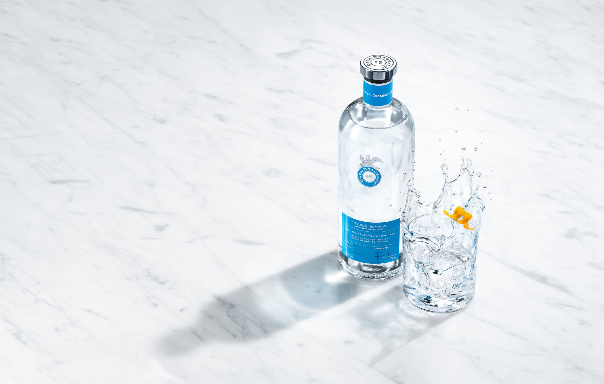 cocktail 桌布 壁紙 — 一個透明伏特加酒瓶和玻璃杯，帶有柑橘飛濺，放在白色大理石表面上，光線明亮。