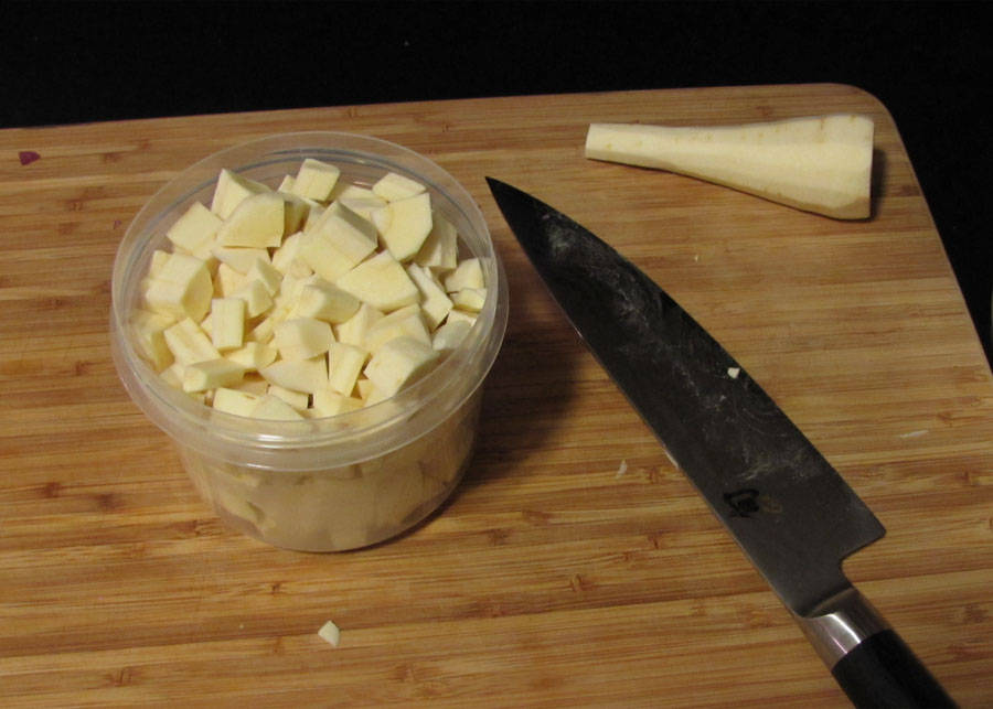 Parsnip 桌布 壁紙 — 一個透明容器裝滿了切成丁的淡黃色歐洲防風草，放在木製砧板上，旁邊有一把用過的廚師刀和一條歐洲防風草根。