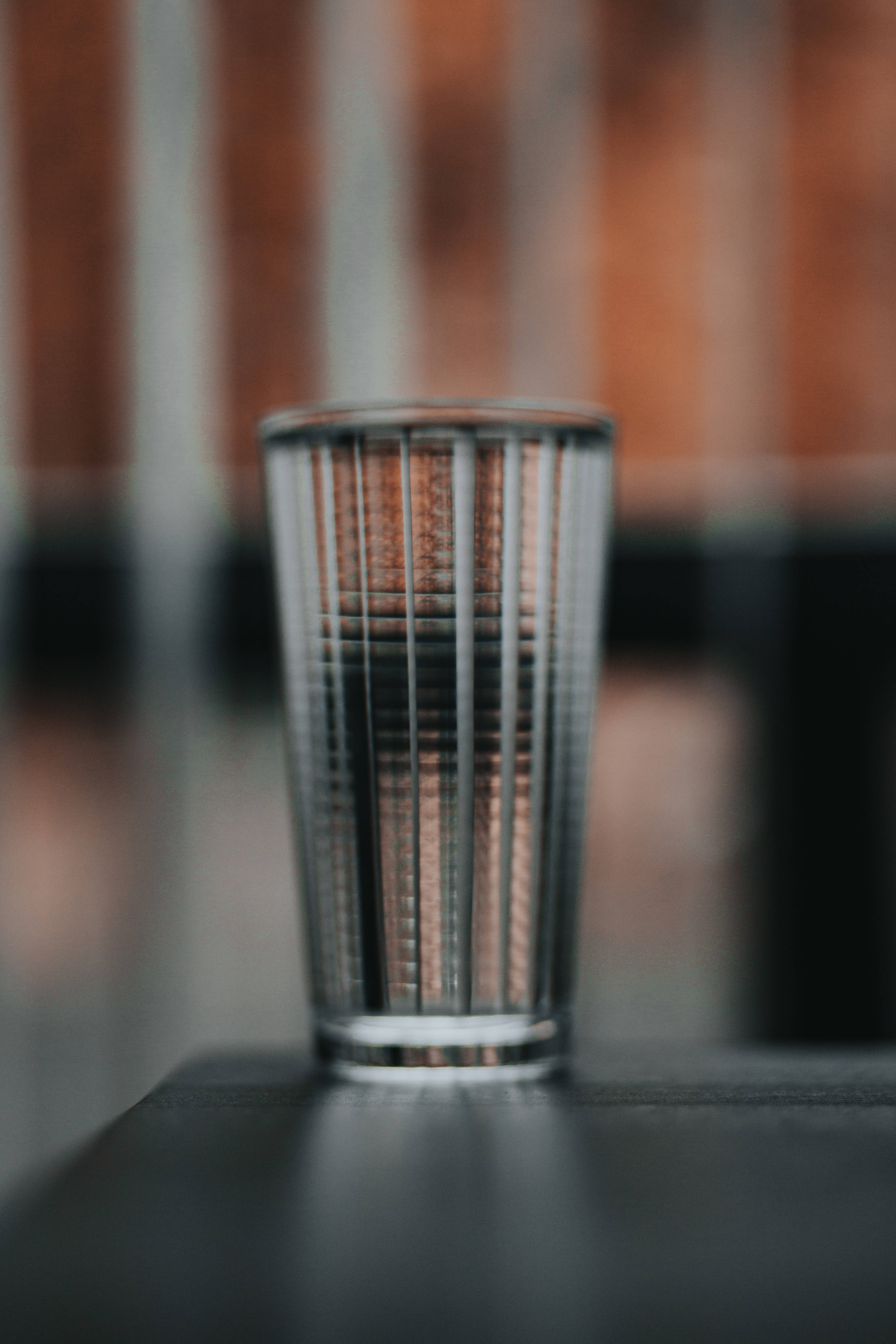 焦點 桌布 壁紙 — 一個透明帶棱紋的飲水杯放在深色表面上，背景是模糊的磚牆。