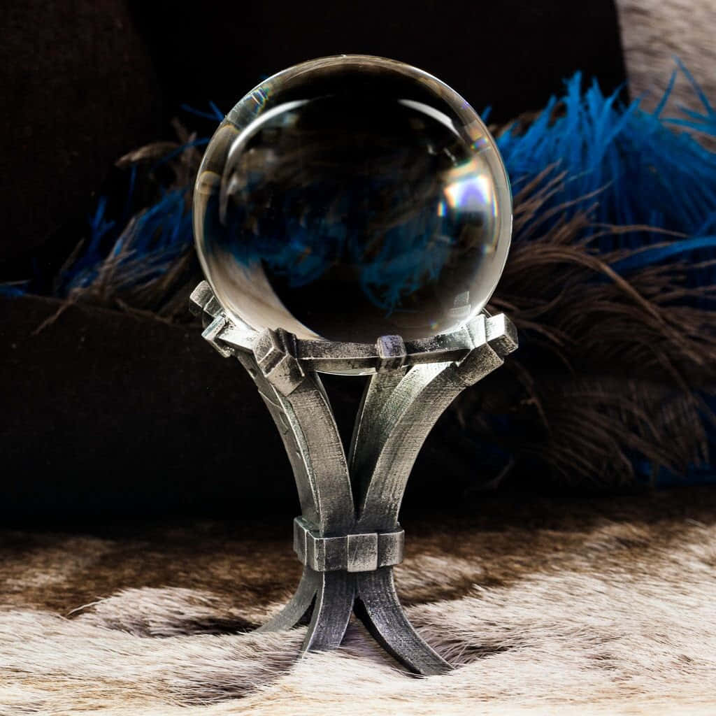Crystal Ball 桌布 壁紙 — 一個透明水晶球放在一個華麗的銀架上，置於毛絨表面，背景有藍色羽毛。