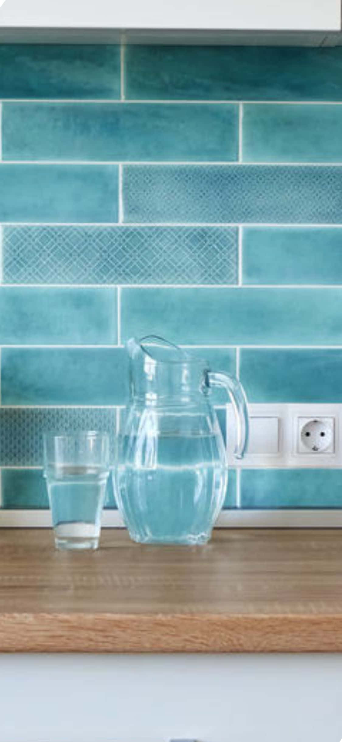 Kitchen Design 桌布 壁紙 — 一個透明玻璃壺和裝滿水的玻璃杯放在木製檯面上，背景是帶有幾何圖案的青綠色瓷磚牆。
