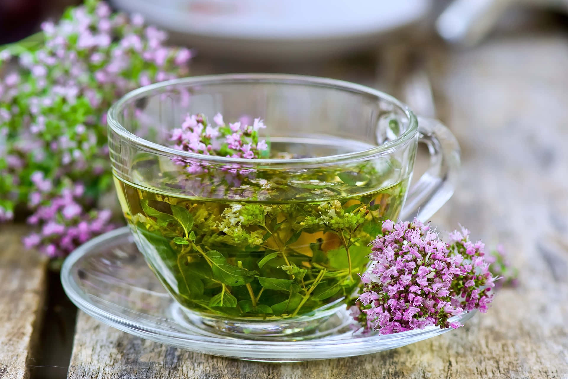 玻璃杯草本茶，漂浮著葉片和紫色花朵，置於木質表面。 — 咖啡動圖 壁紙