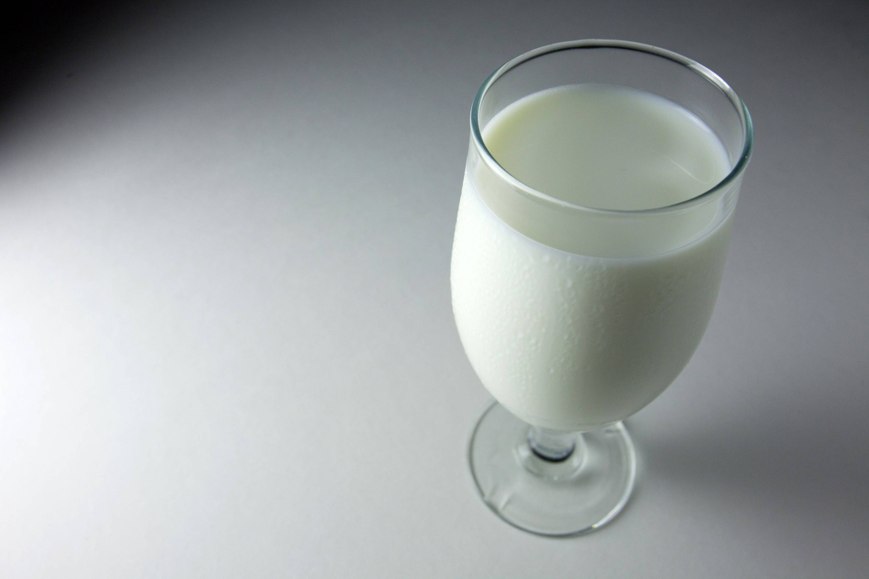 Milk 桌布 壁紙 — 一個透明玻璃杯裝滿冰牛奶，放在光滑的灰色表面上，在柔和的工作室燈光下。
