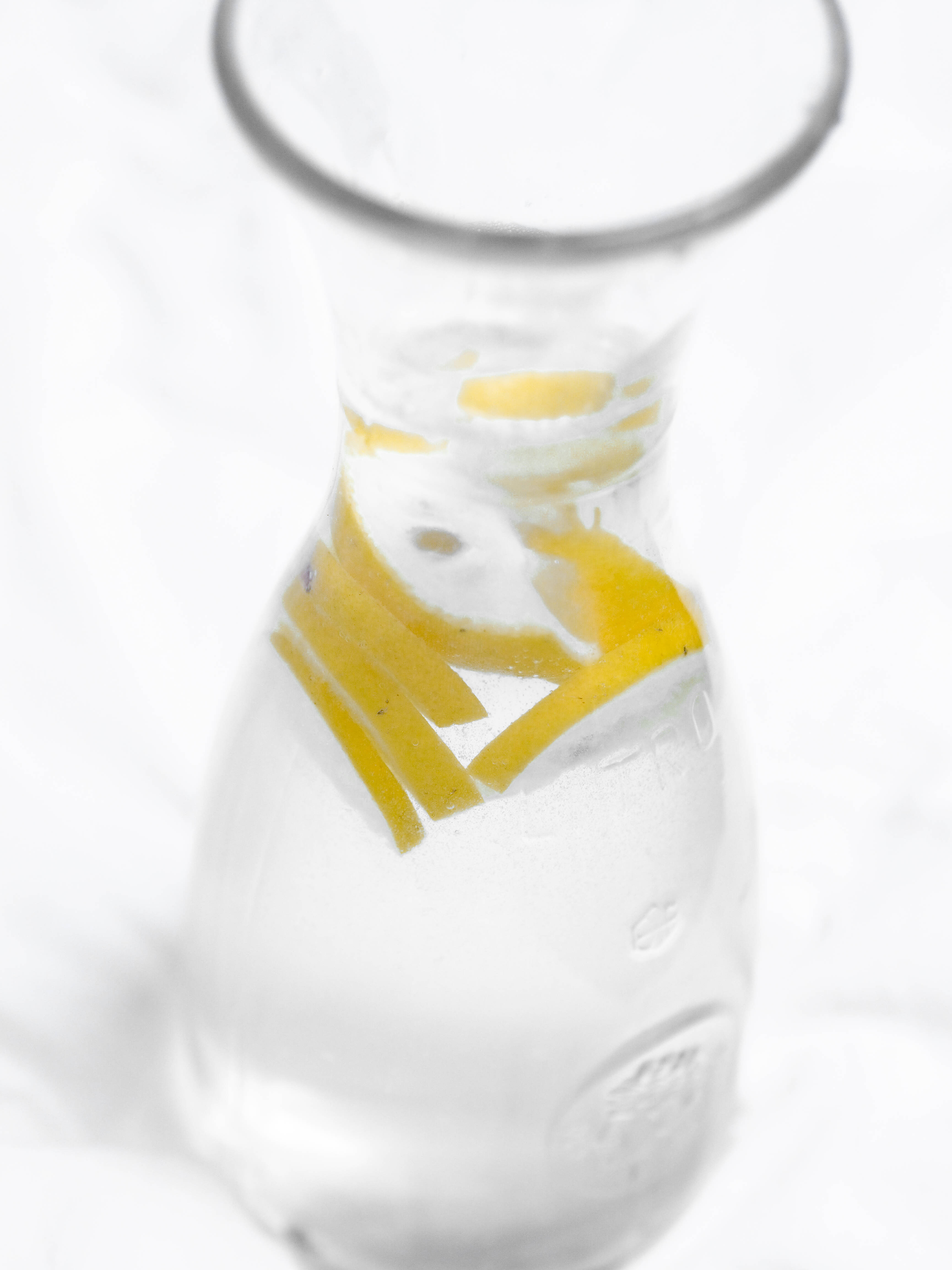Pinterest 桌布 壁紙 — 一個透明玻璃水瓶，裝滿水和鮮黃色檸檬片，襯托在柔和的白色背景上。