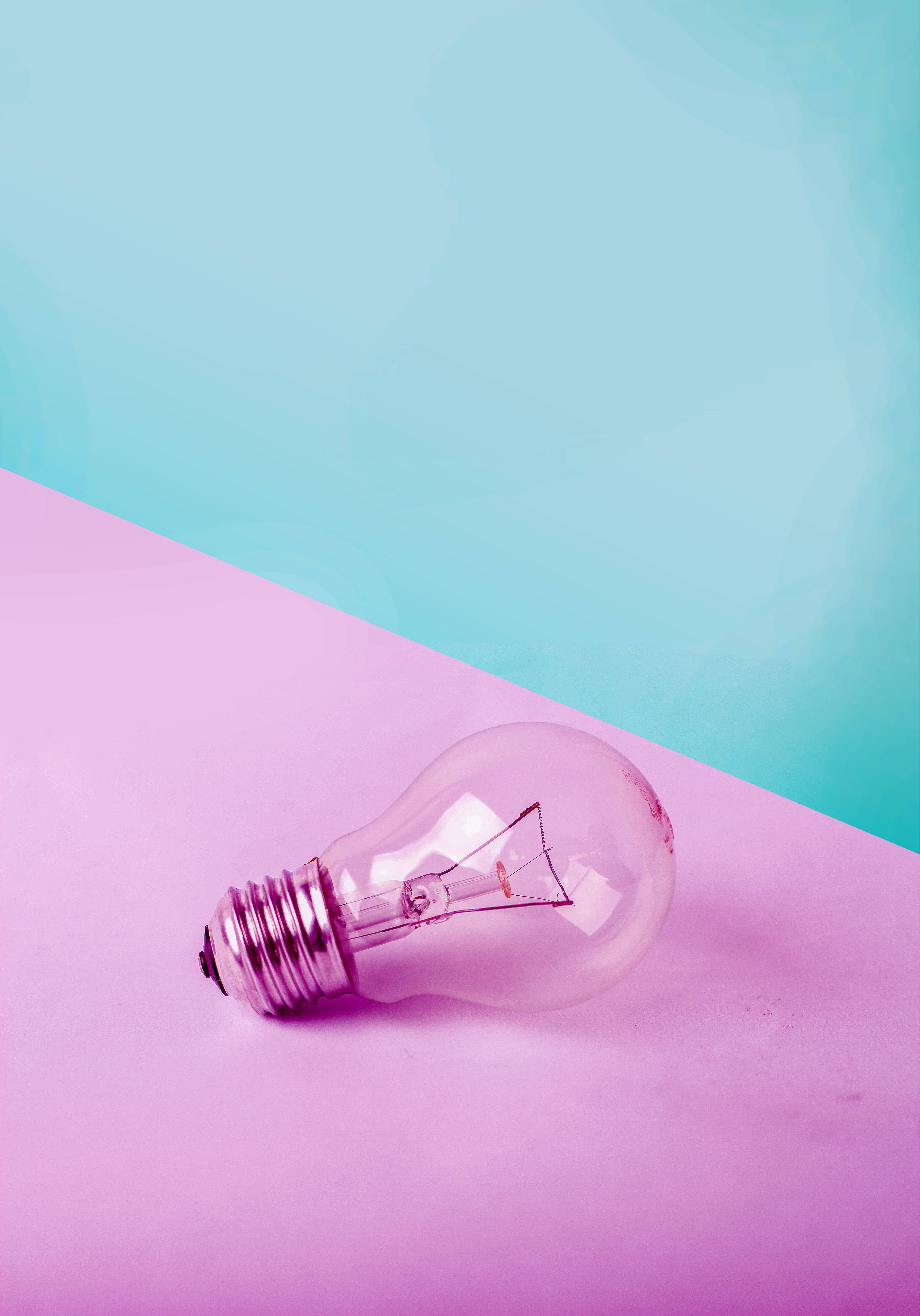 Light Bulb 桌布 壁紙 — 一個透明玻璃燈泡放在充滿活力的粉紅色表面上，背景是柔和的青綠色，構成極簡風格。