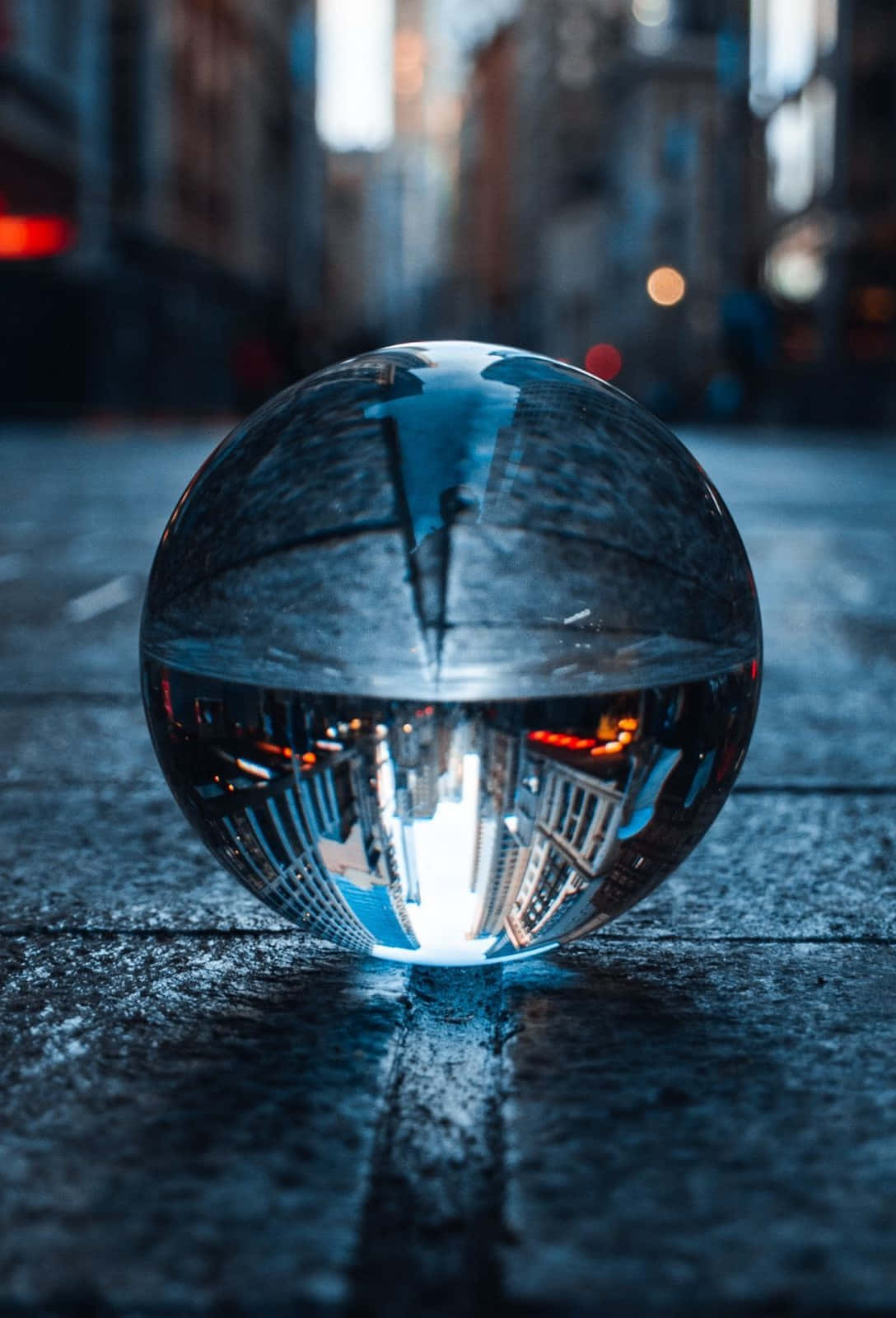 Crystal Ball 桌布 壁紙 — 一個透明玻璃球放在潮濕的路面上，反射出暮色中模糊的城市景觀和閃爍的燈光。