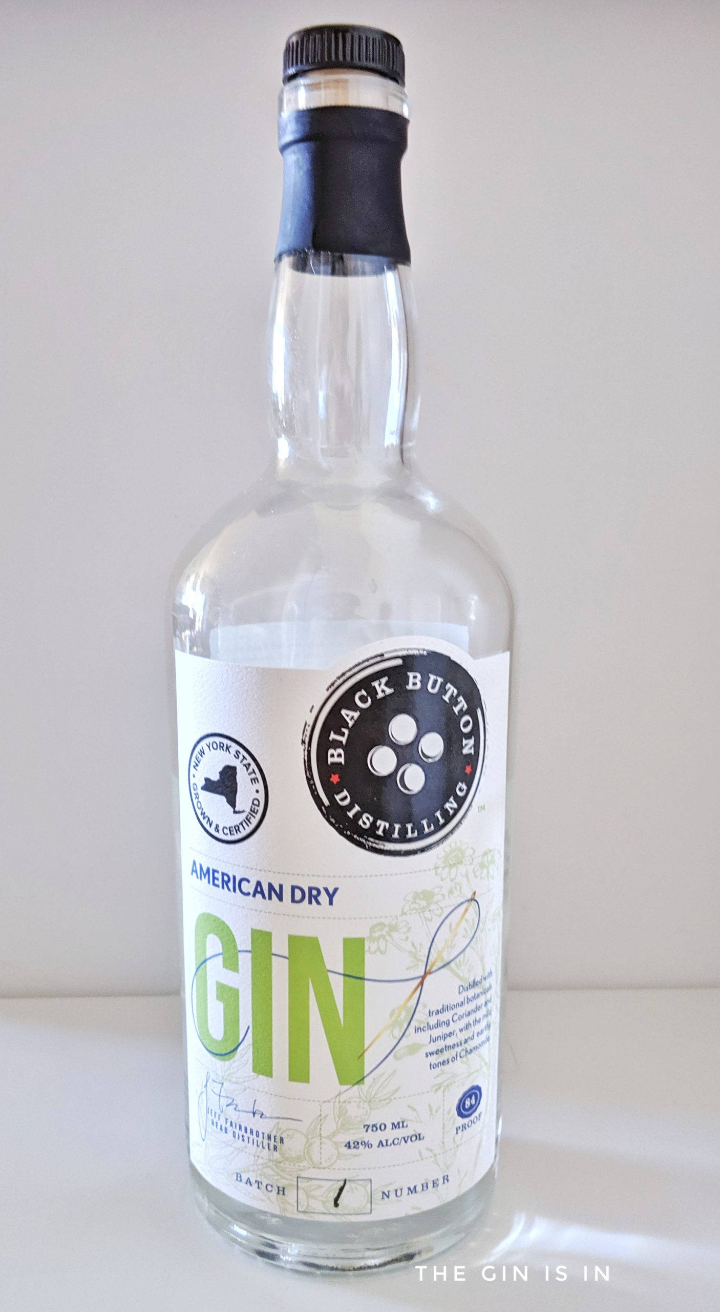 alcohol 桌布 壁紙 — 一個透明玻璃瓶的 Black Button Distilling American Dry Gin 直立於白色表面上，背景簡潔。