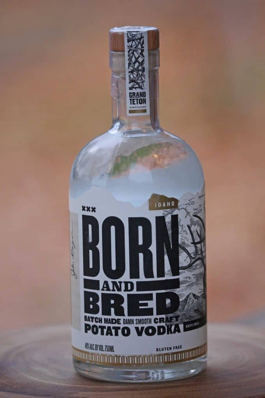 bottle 桌布 壁紙 — 一個透明玻璃瓶的 Born and Bred 馬鈴薯伏特加，置於木質表面上，背景溫暖模糊。