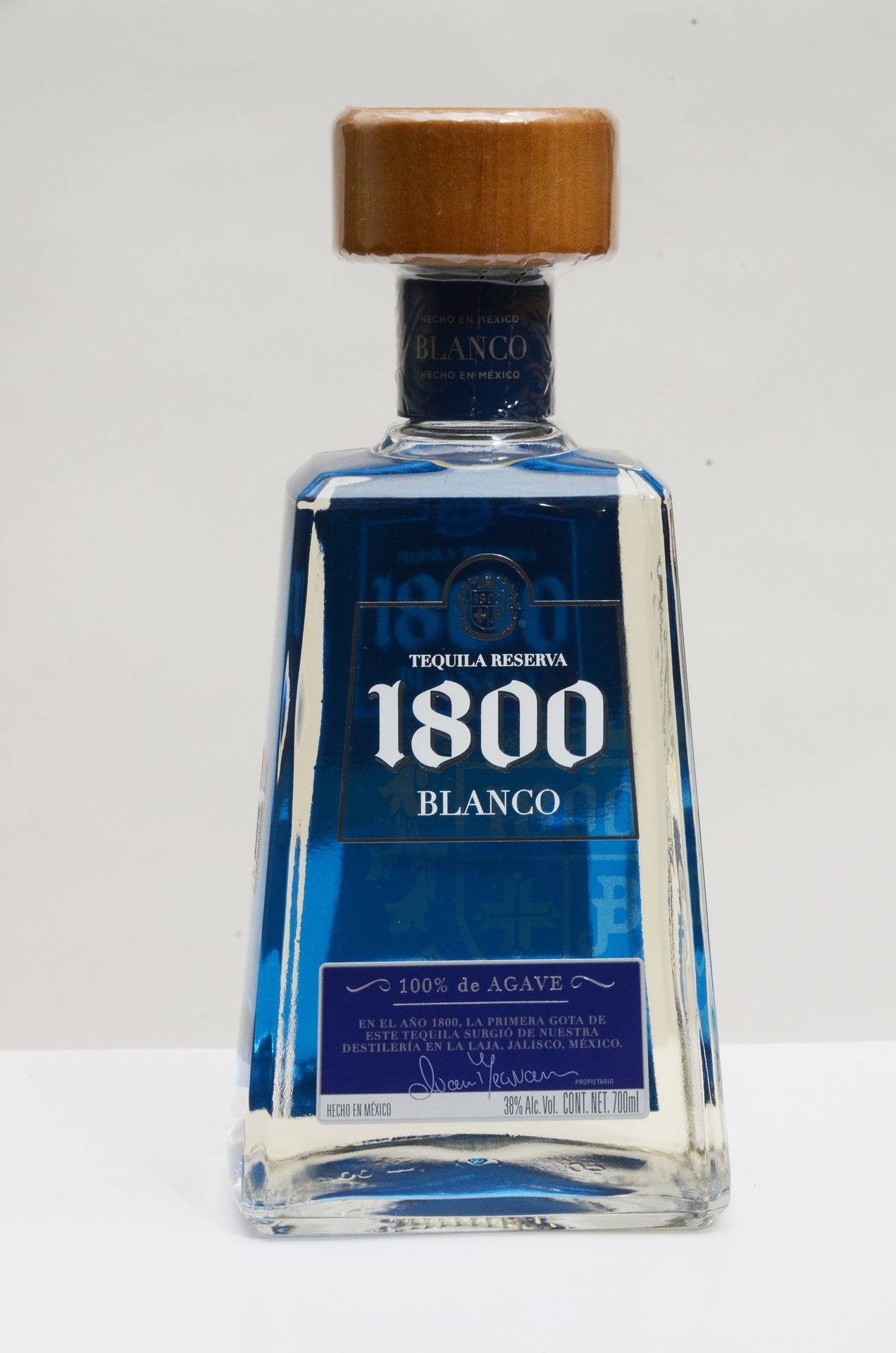 alcohol 桌布 壁紙 — 一個透明玻璃瓶的1800 Blanco龍舌蘭酒，帶有藍色標籤和木蓋，居中放置在純白色背景上。