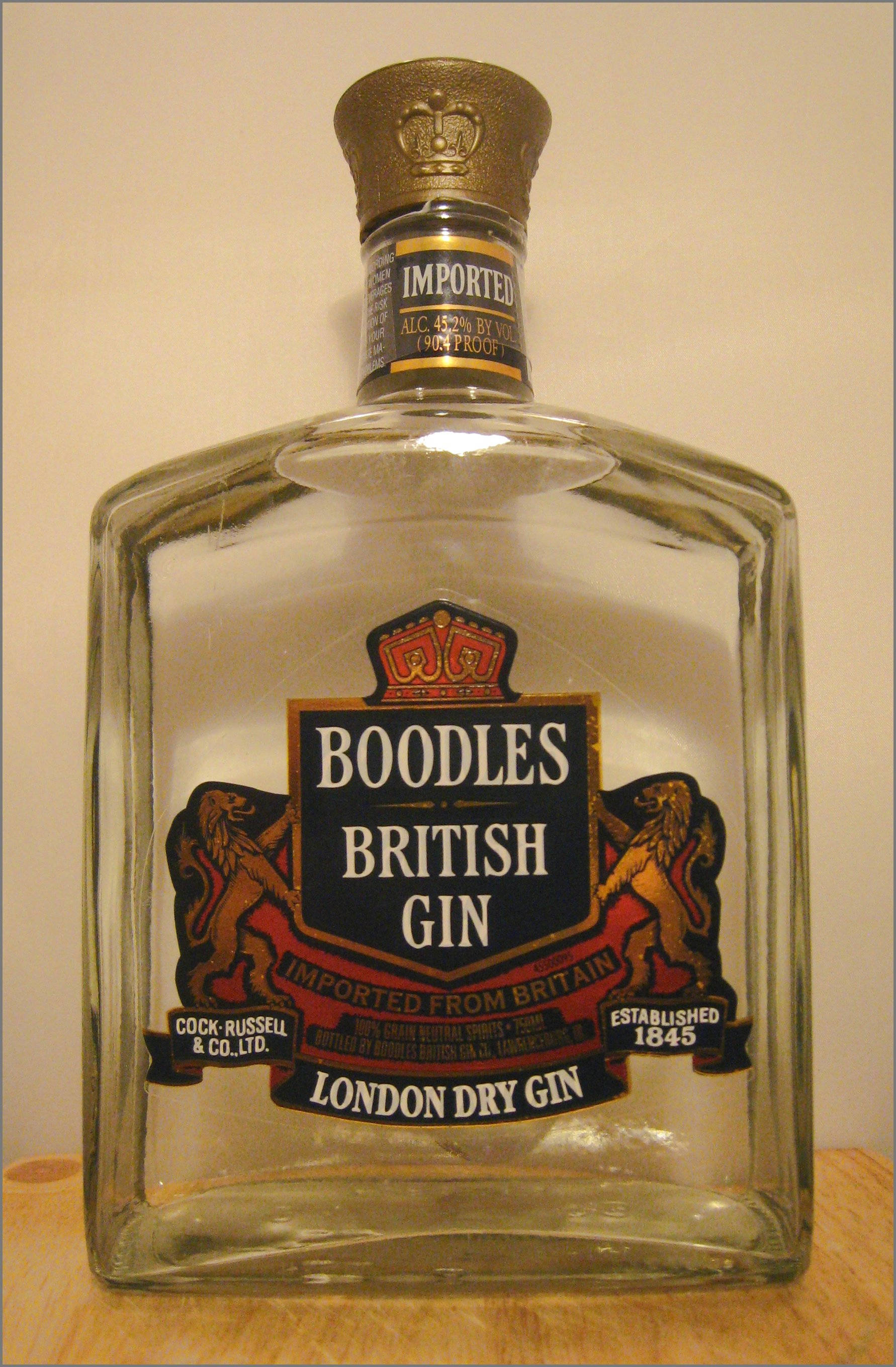 classic 桌布 壁紙 — 一個透明玻璃瓶的Boodles British Gin，帶有金色瓶蓋和裝飾有獅子與皇冠的華麗標籤，放置在木質表面上。