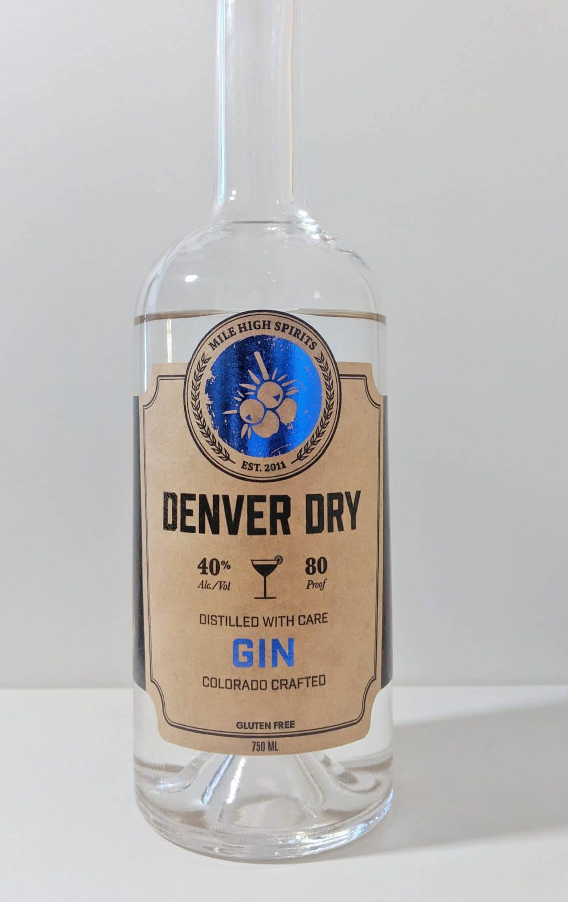 drinks 桌布 壁紙 — 一個透明玻璃瓶的Denver Dry Gin，帶有質樸的棕色標籤和藍色標誌，立在純白色背景前。
