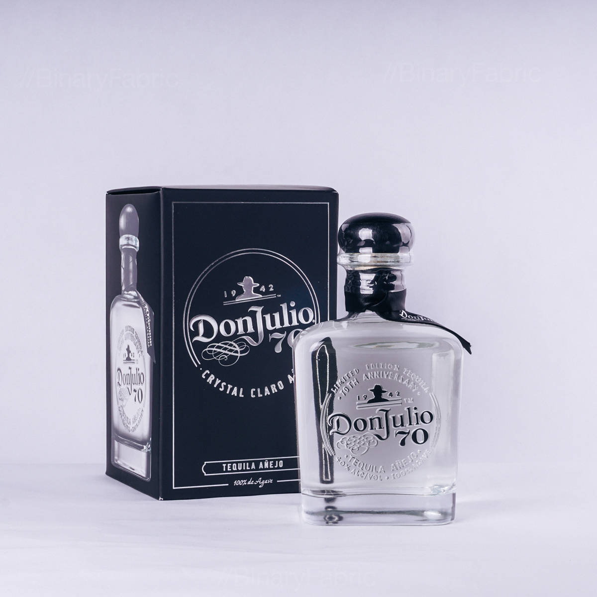 Box 桌布 壁紙 — 一個透明玻璃瓶的Don Julio 70龍舌蘭酒放在其黑色盒子旁邊，背景為純白色。