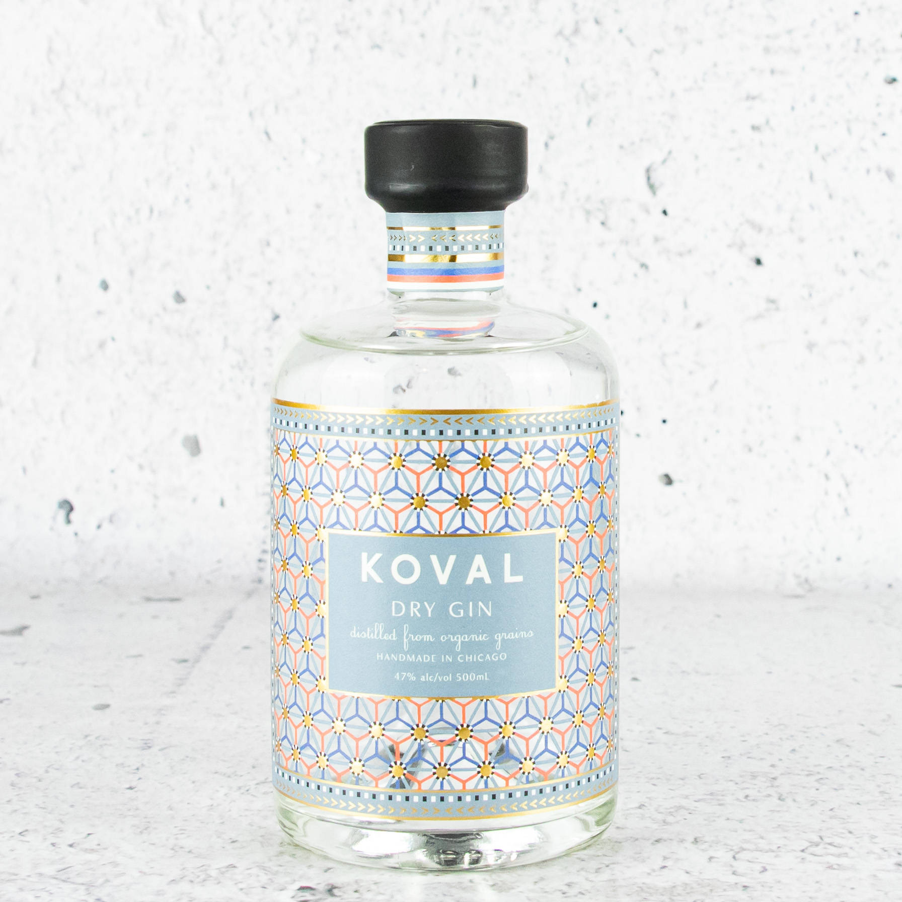 alcohol 桌布 壁紙 — 一個透明玻璃瓶的Koval Dry Gin，帶有幾何圖案標籤，放在有斑點的白色表面上，背景是紋理牆壁。