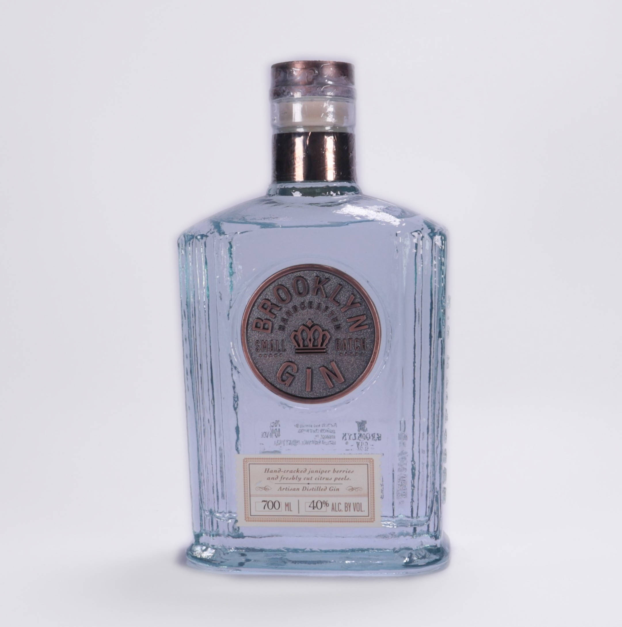 alcohol 桌布 壁紙 — 一個透明玻璃瓶的布魯克林小批量琴酒，帶有銅蓋和壓花標籤，立在純白色背景前。