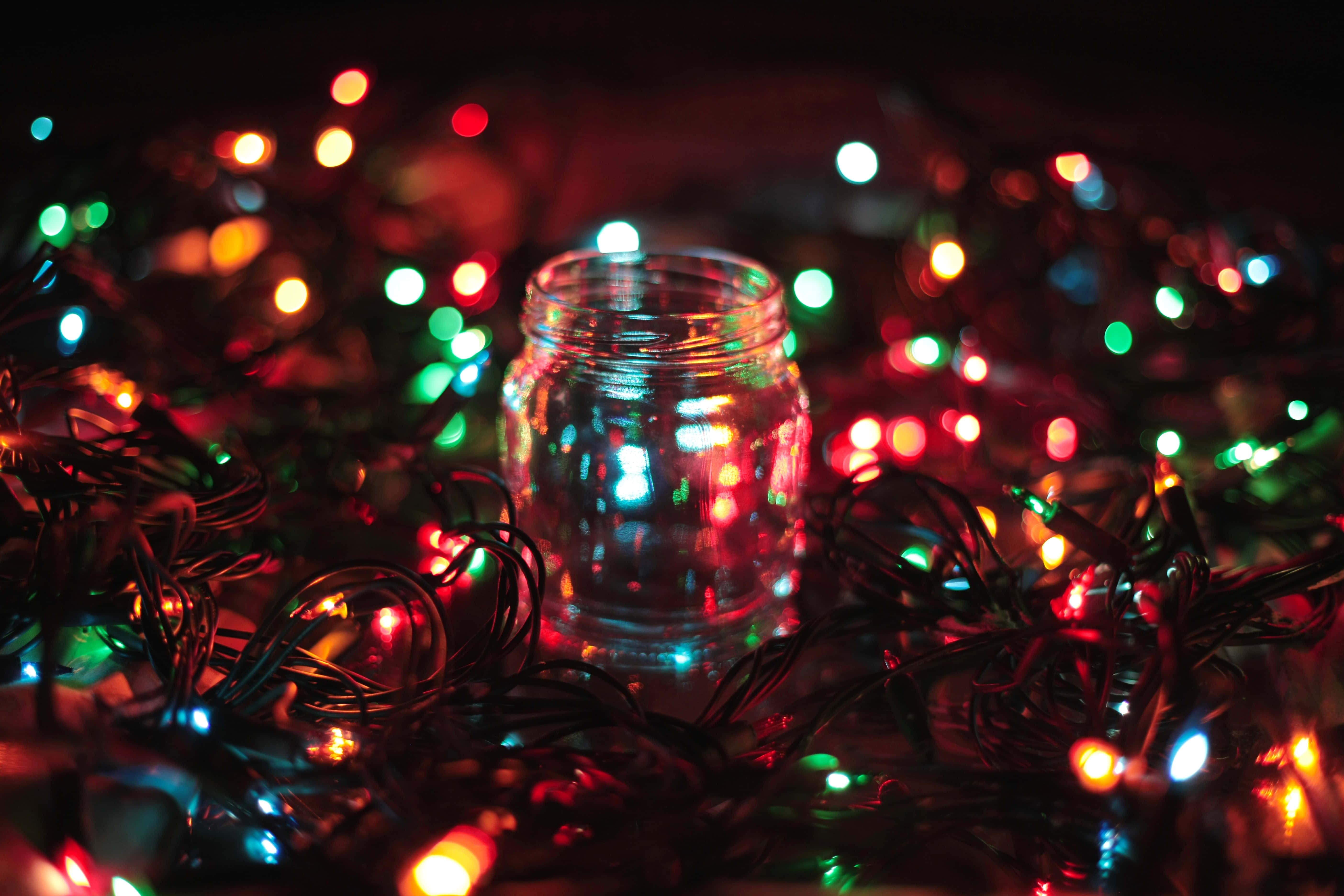 Christmas Light 桌布 壁紙 — 一個透明玻璃瓶被纏繞的彩色童話燈包圍，在黑暗環境中柔和發光。