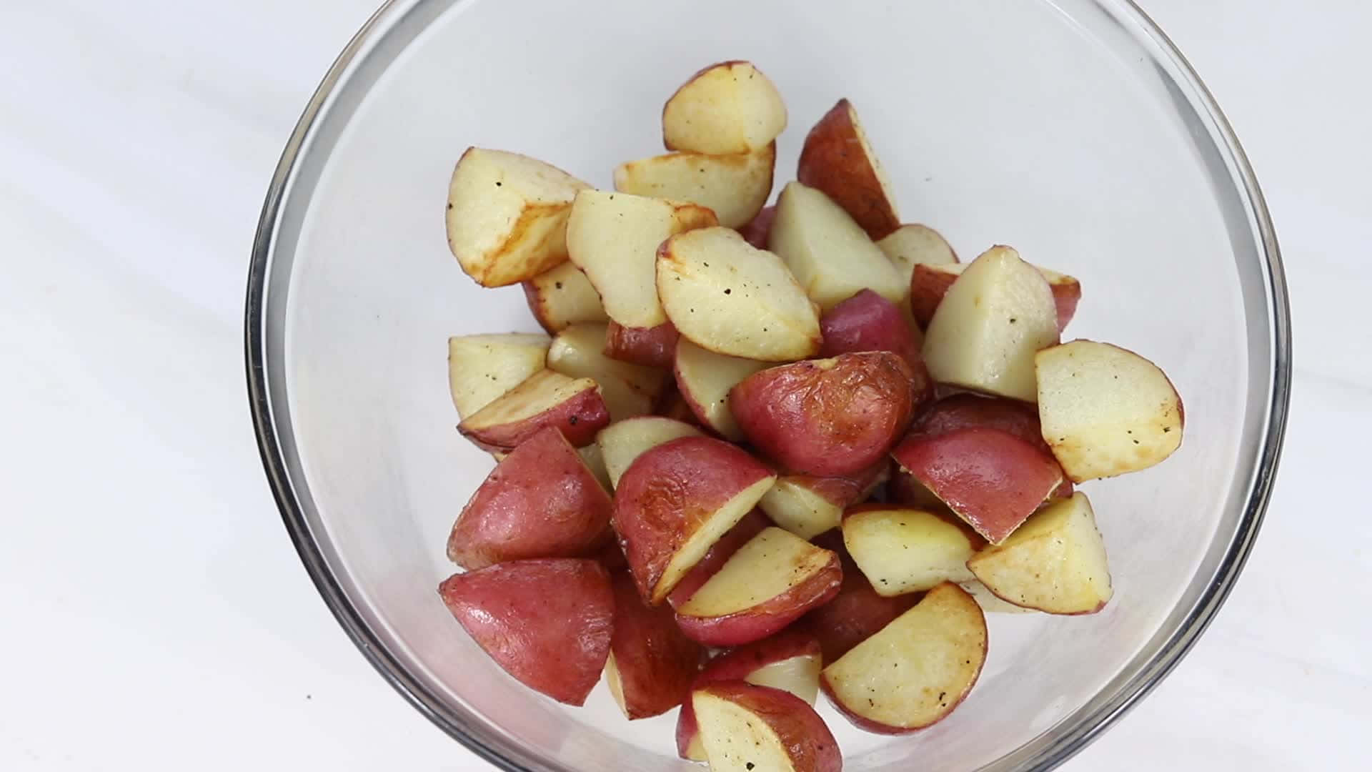 Red Potatoes 桌布 壁紙 — 一個透明玻璃碗盛裝著烤紅薯，邊緣呈金黃色，可見調味料，背景為白色大理石。