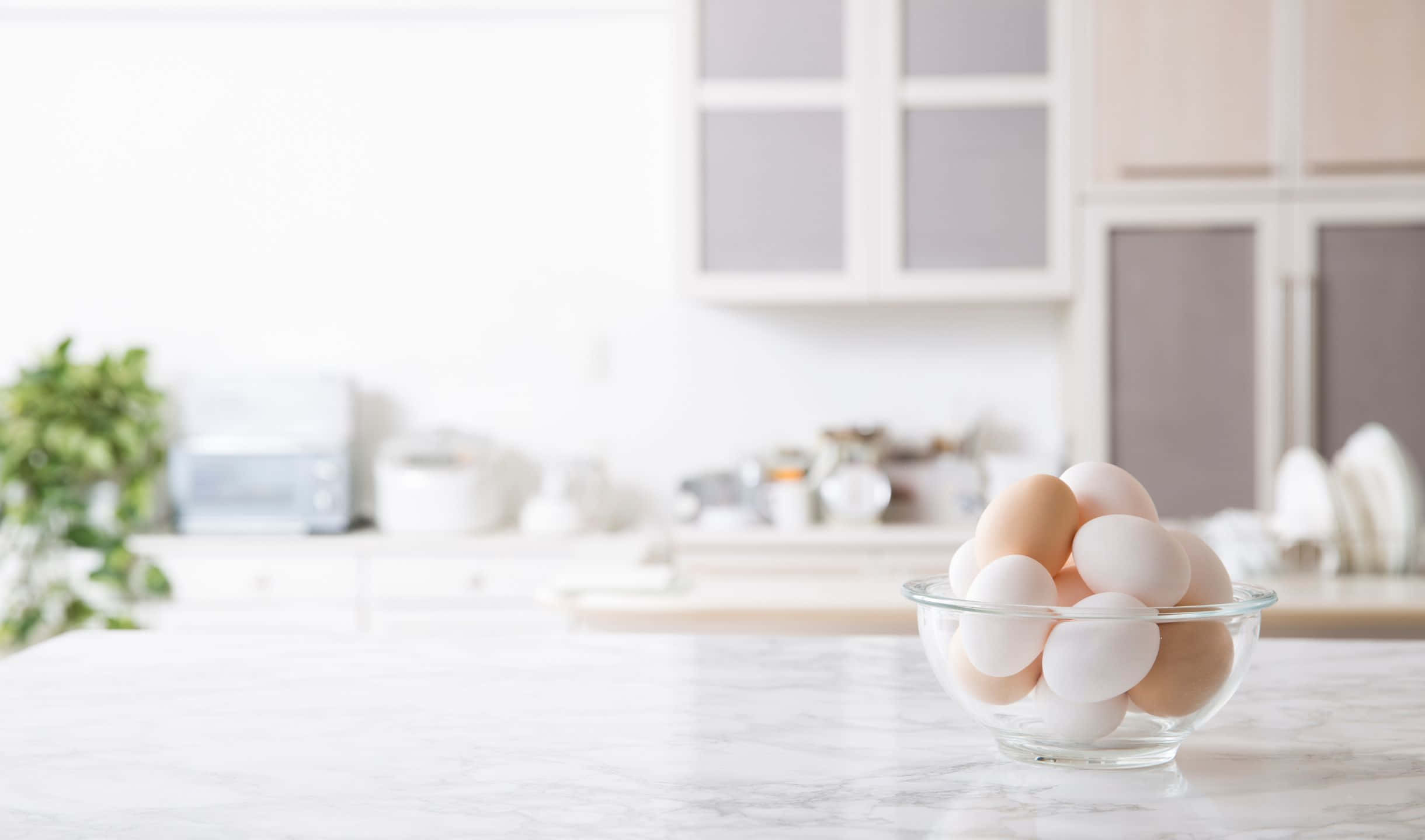 kitchen 桌布 壁紙 — 一個透明玻璃碗裝滿白色和棕色雞蛋，放在大理石廚房檯面上，伴隨著柔和自然光。