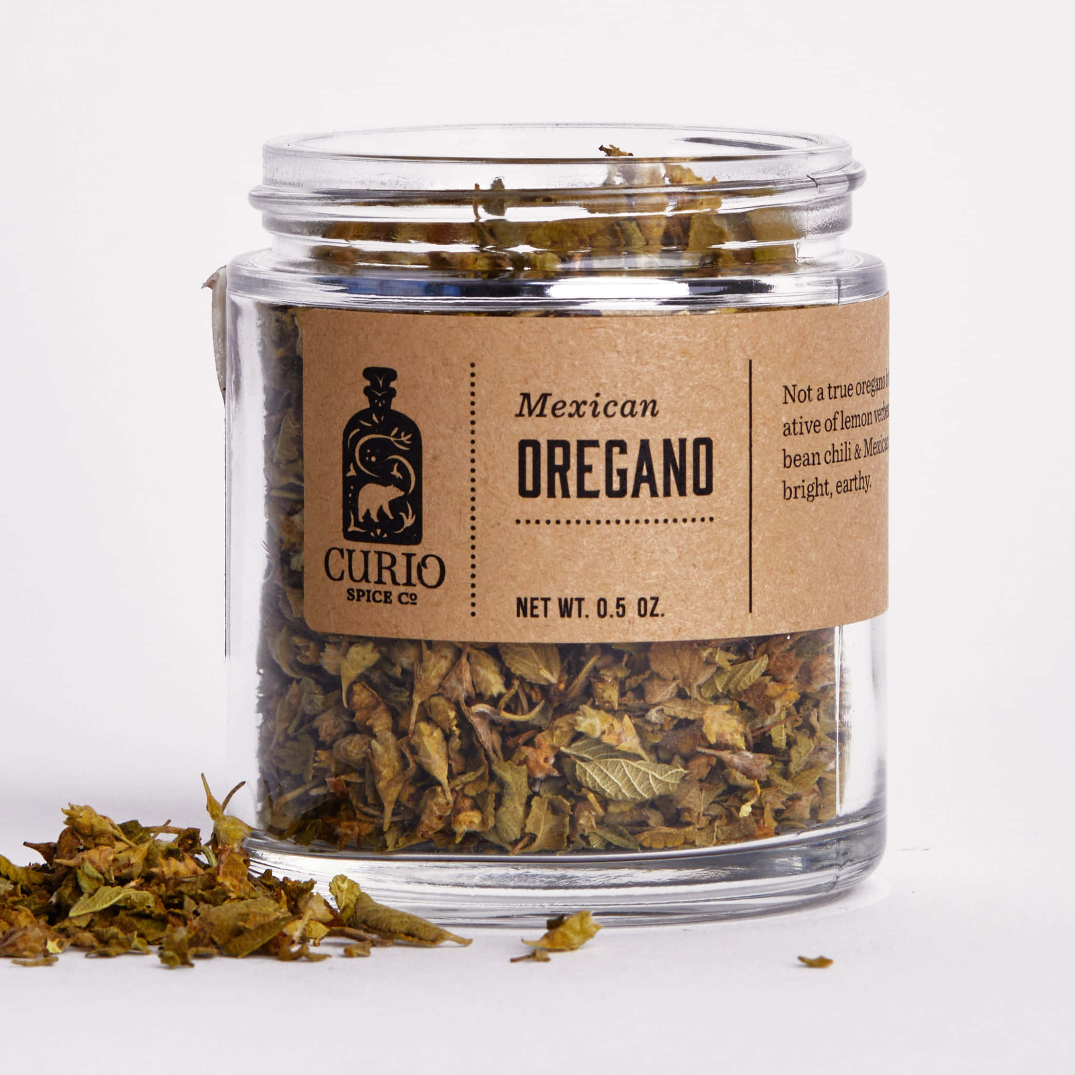 Mexican 桌布 壁紙 — 一個透明玻璃罐裝滿乾燥墨西哥牛至，放在白色背景前，附近散落著葉子。