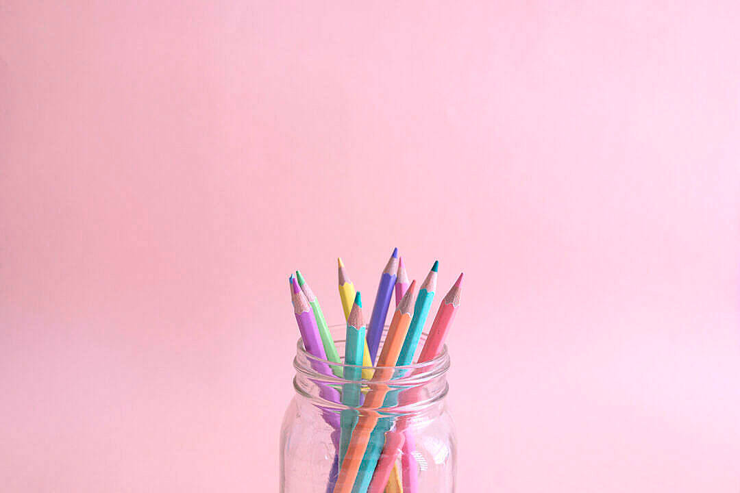 Pastel Pink Aesthetic 桌布 壁紙 — 一個透明玻璃罐裝滿了色彩繽紛的削尖鉛筆，放在柔和的粉紅色背景前。