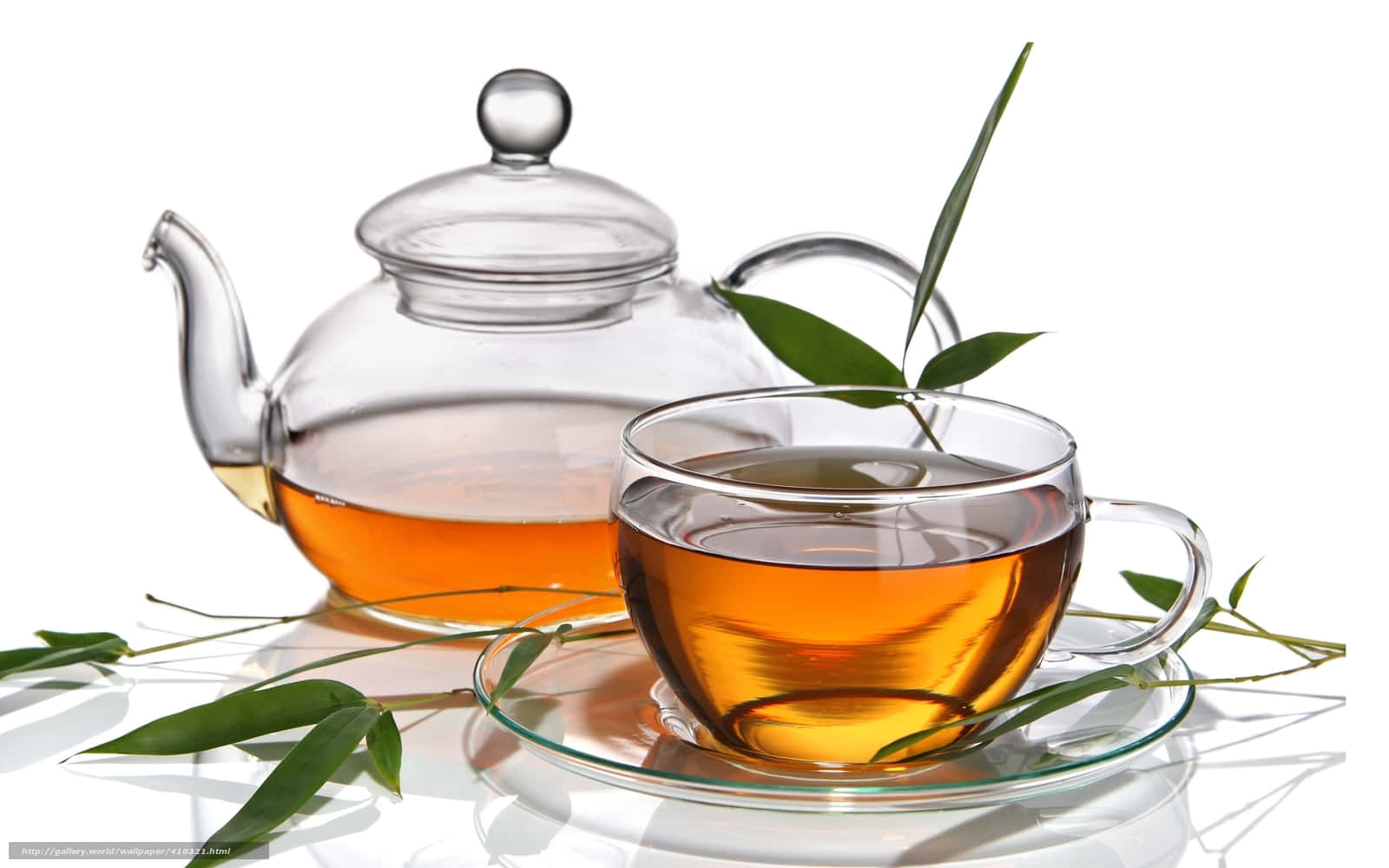 咖啡動圖 桌布 壁紙 — 一個透明玻璃茶壺和杯子，裝滿琥珀色茶，周圍是新鮮的綠色竹葉，放在白色反光表面上。