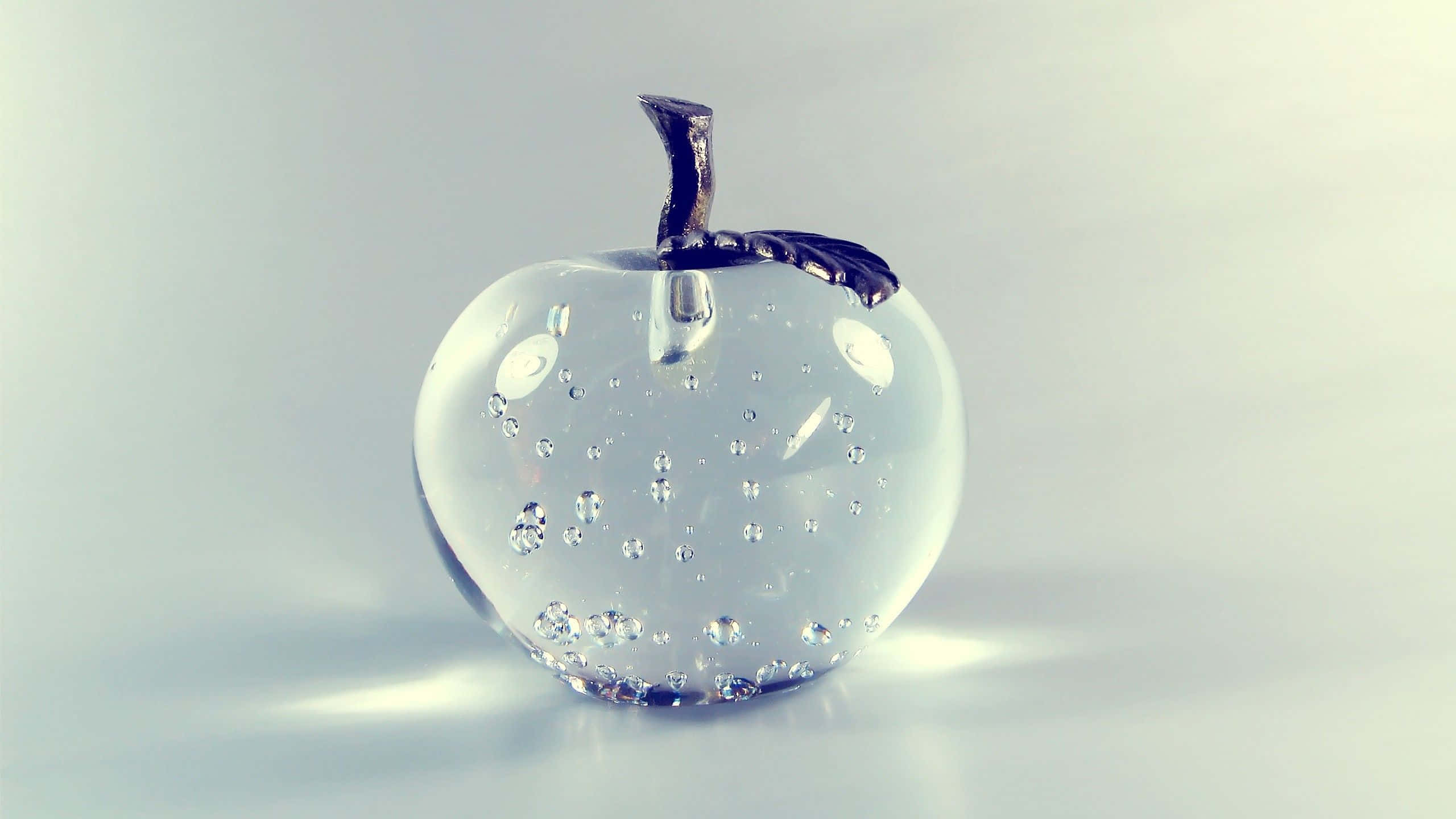 Transparent 桌布 壁紙 — 一個透明玻璃蘋果雕塑，內嵌氣泡和深色莖，放置在柔和燈光下的反光表面上。