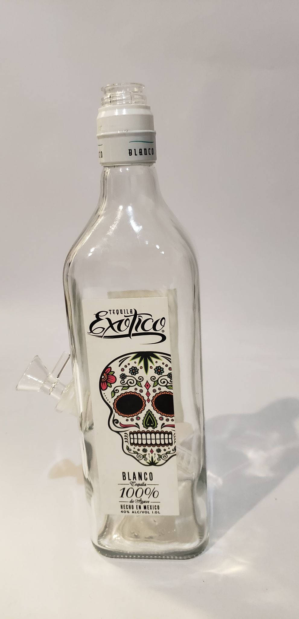 bottle 桌布 壁紙 — 一個透明玻璃龍舌蘭酒瓶，帶有糖骷髏標籤，立在純白色背景前。