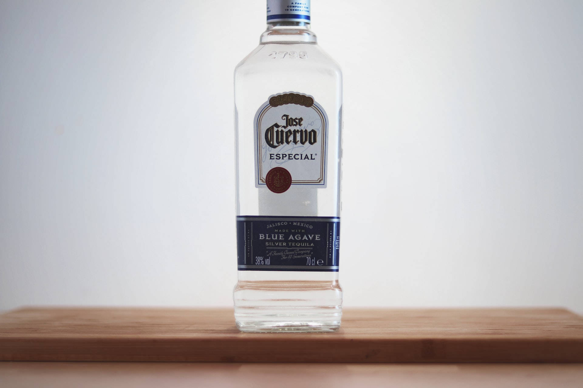 alcohol 桌布 壁紙 — 一個透明的 Jose Cuervo Especial Silver Tequila 酒瓶，置中放在淺色木質表面上，背景為純白色。