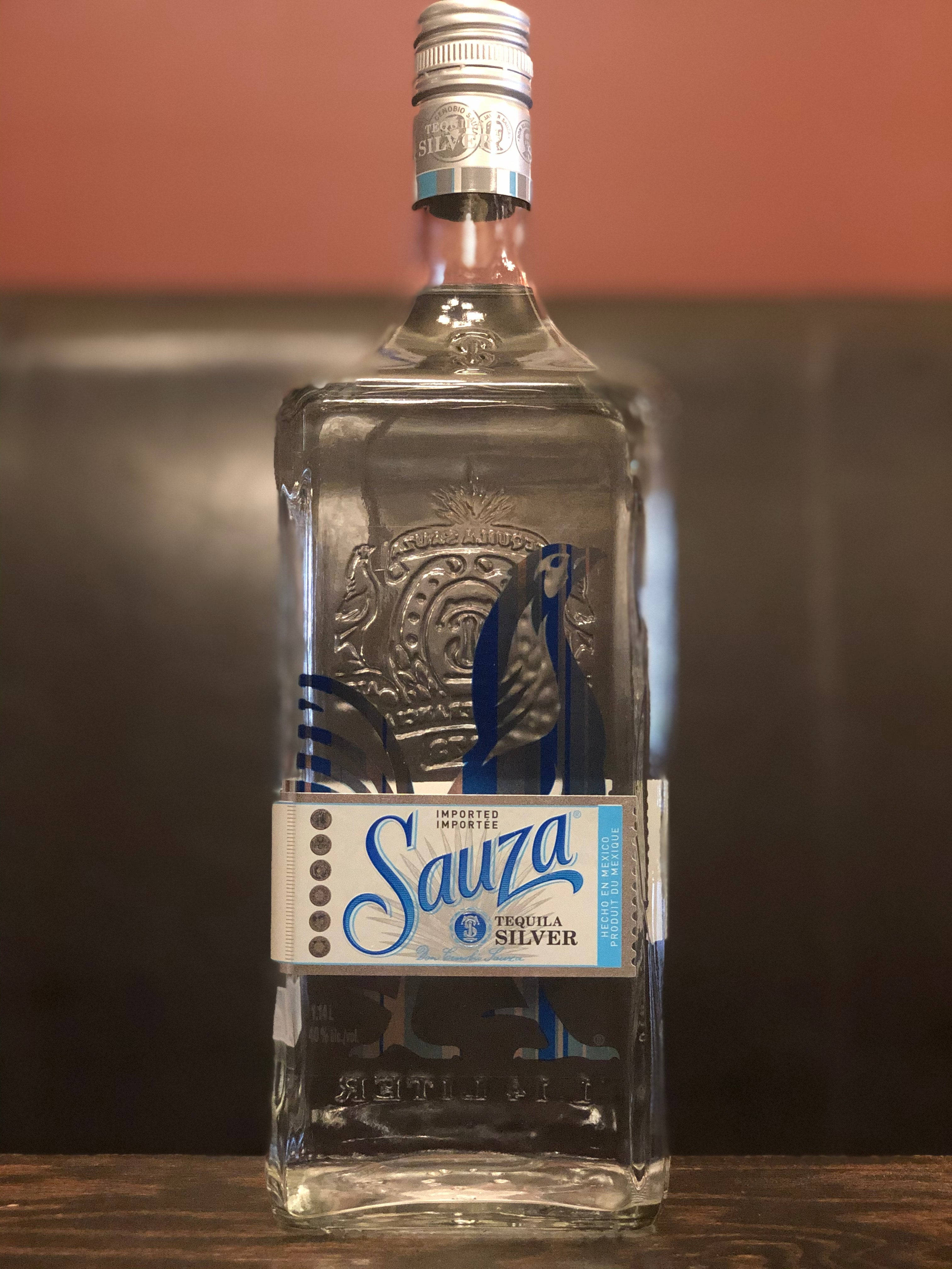 alcohol 桌布 壁紙 — 一個透明的 Sauza Silver Tequila 酒瓶，帶有藍色和銀色品牌標識，置中放在木質表面上，背景是暖色調的牆壁。