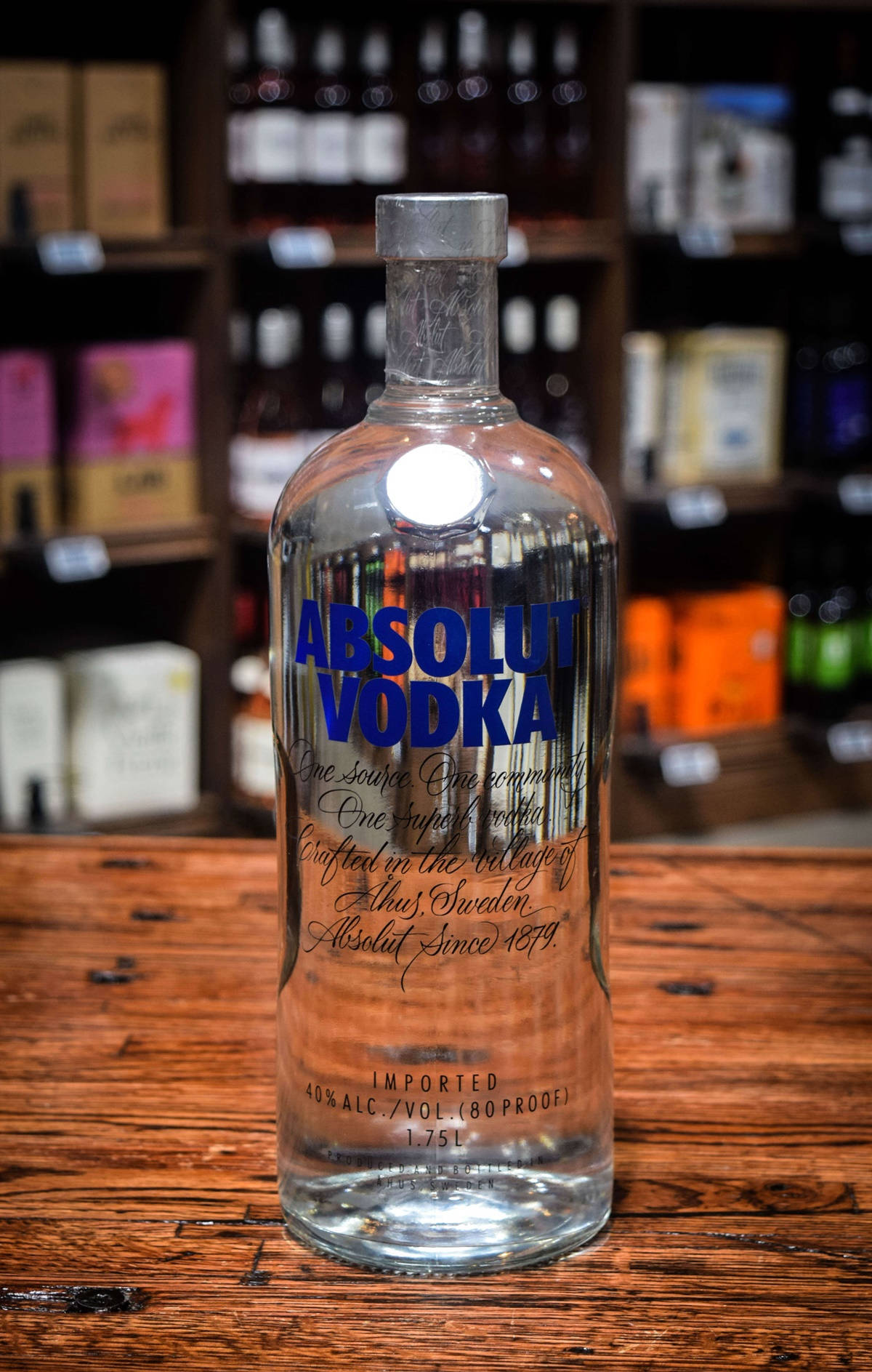 bottle 桌布 壁紙 — 一個透明的Absolut Vodka瓶子，上面有藍色字，放在鄉村風格的木吧檯中央，背景是放滿酒的架子。