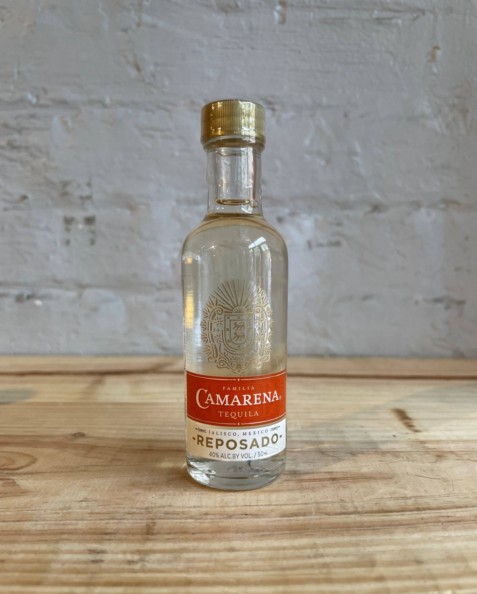 Tequila 桌布 壁紙 — 一個透明的Camarena Reposado龍舌蘭酒瓶，金色瓶蓋，放在鄉村風格的木桌中央，背景是白色磚牆。