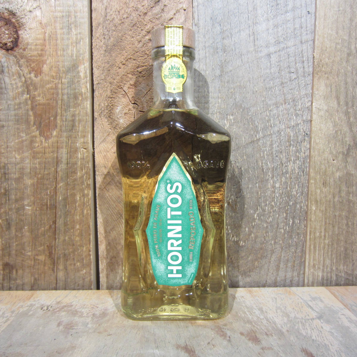 bottle 桌布 壁紙 — 一個透明的Hornitos龍舌蘭酒瓶，帶有綠色標籤，放置在風化的木質表面上，背景是鄉村風格的木質背景。