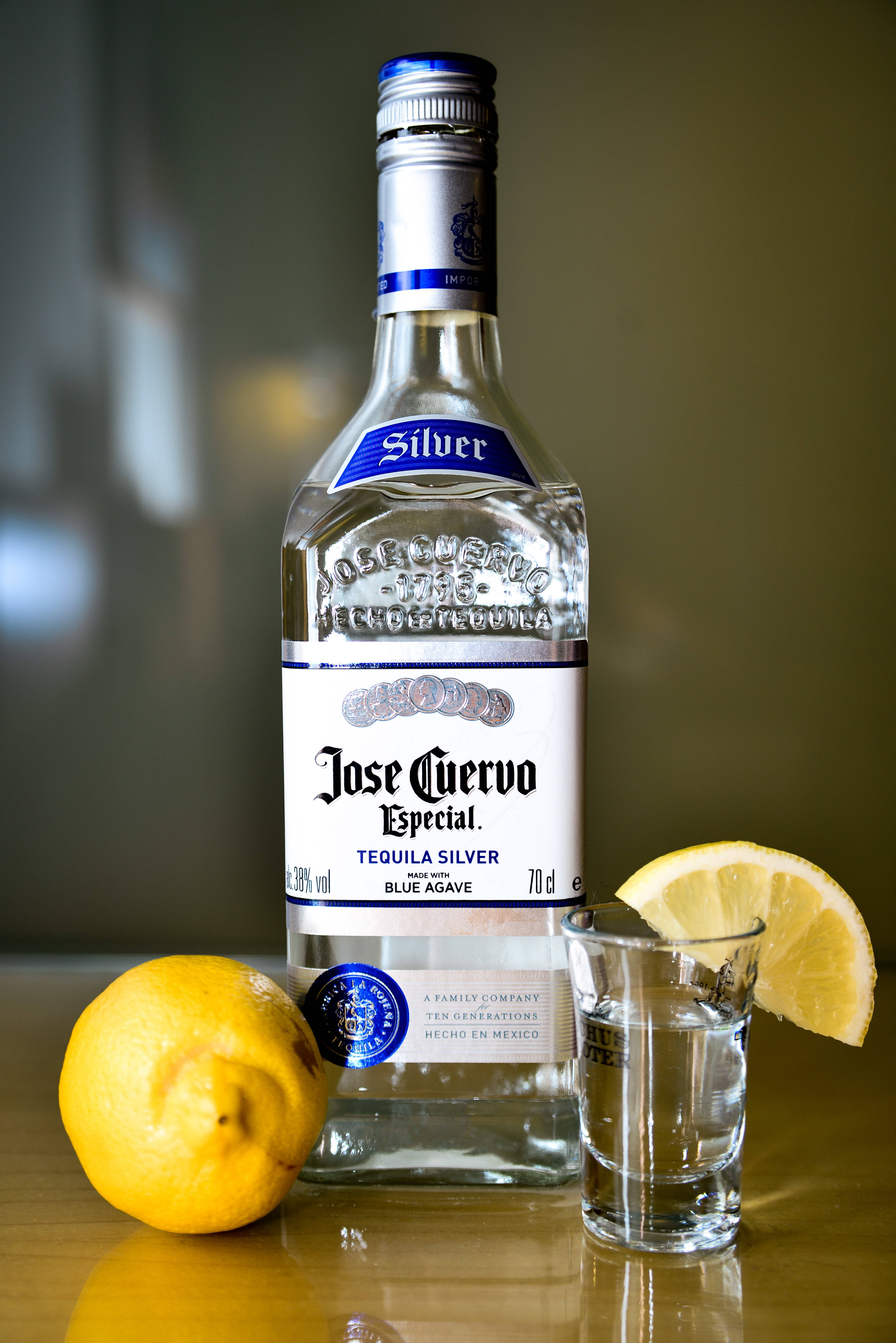 alcohol 桌布 壁紙 — 一個透明的Jose Cuervo Silver龍舌蘭酒瓶放在木桌上，旁邊有一個附有檸檬角和整個檸檬的烈酒杯。