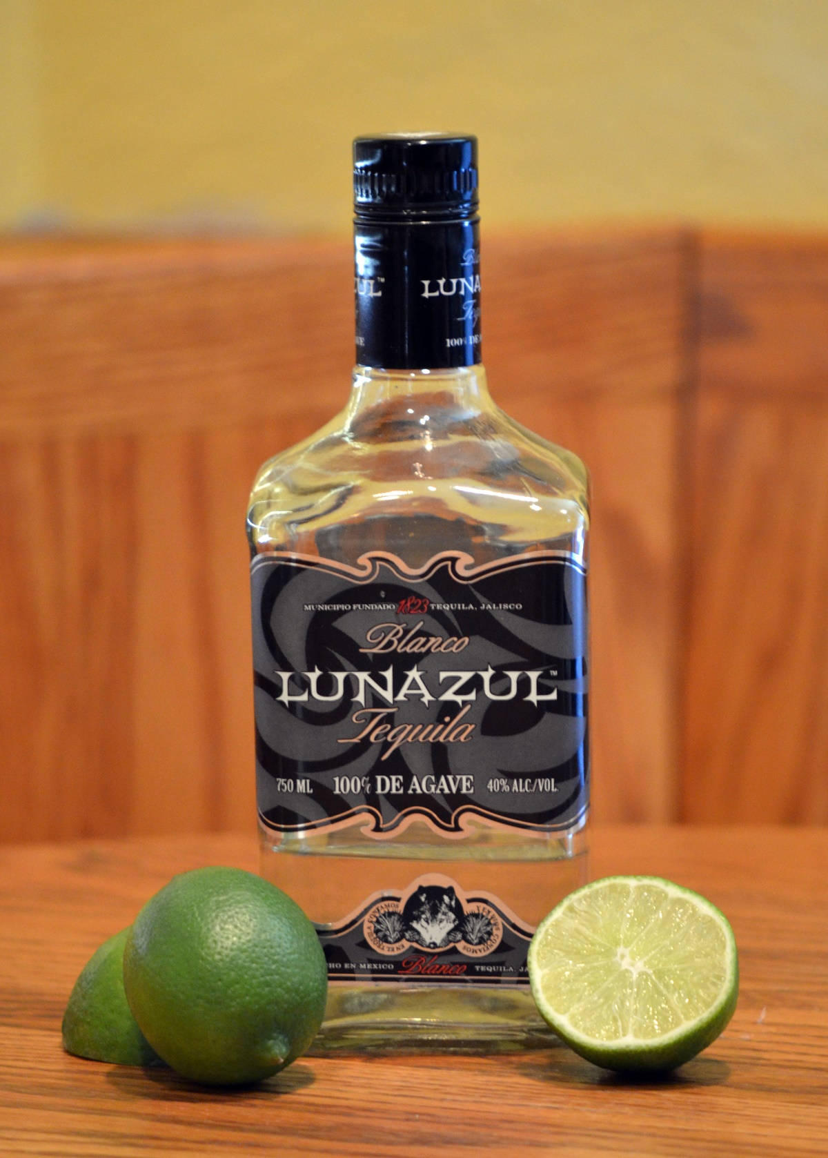 alcohol 桌布 壁紙 — 一個透明的Lunazul Blanco龍舌蘭酒瓶放在木桌上，旁邊有完整和切半的萊姆。