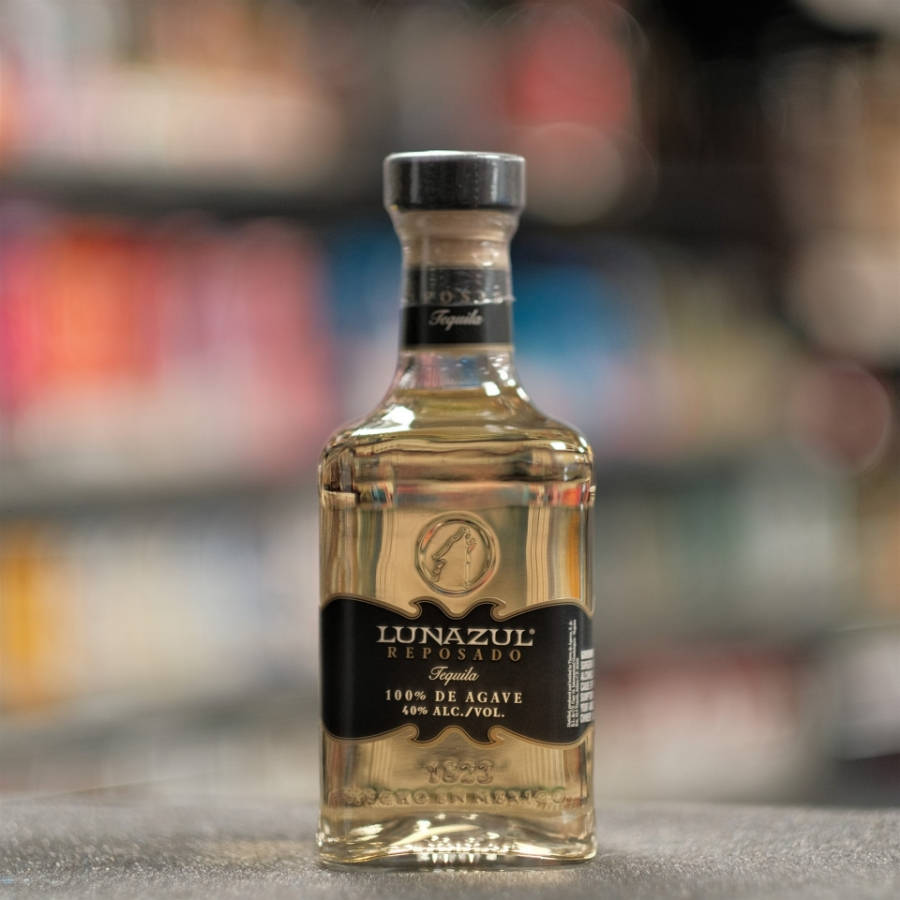 alcohol 桌布 壁紙 — 一個透明的Lunazul Reposado龍舌蘭酒瓶放在灰色表面上，背景是模糊的商店貨架。
