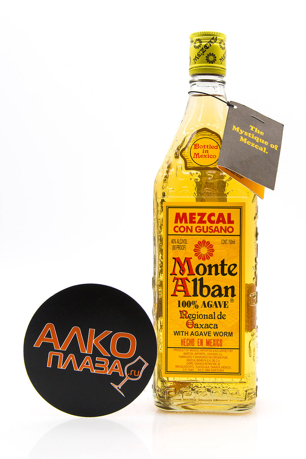 bottle 桌布 壁紙 — 一個透明的Monte Alban Mezcal酒瓶，帶有龍舌蘭蟲和標籤，放在一個帶有橙色西里爾文字的黑色杯墊旁邊，背景為白色。