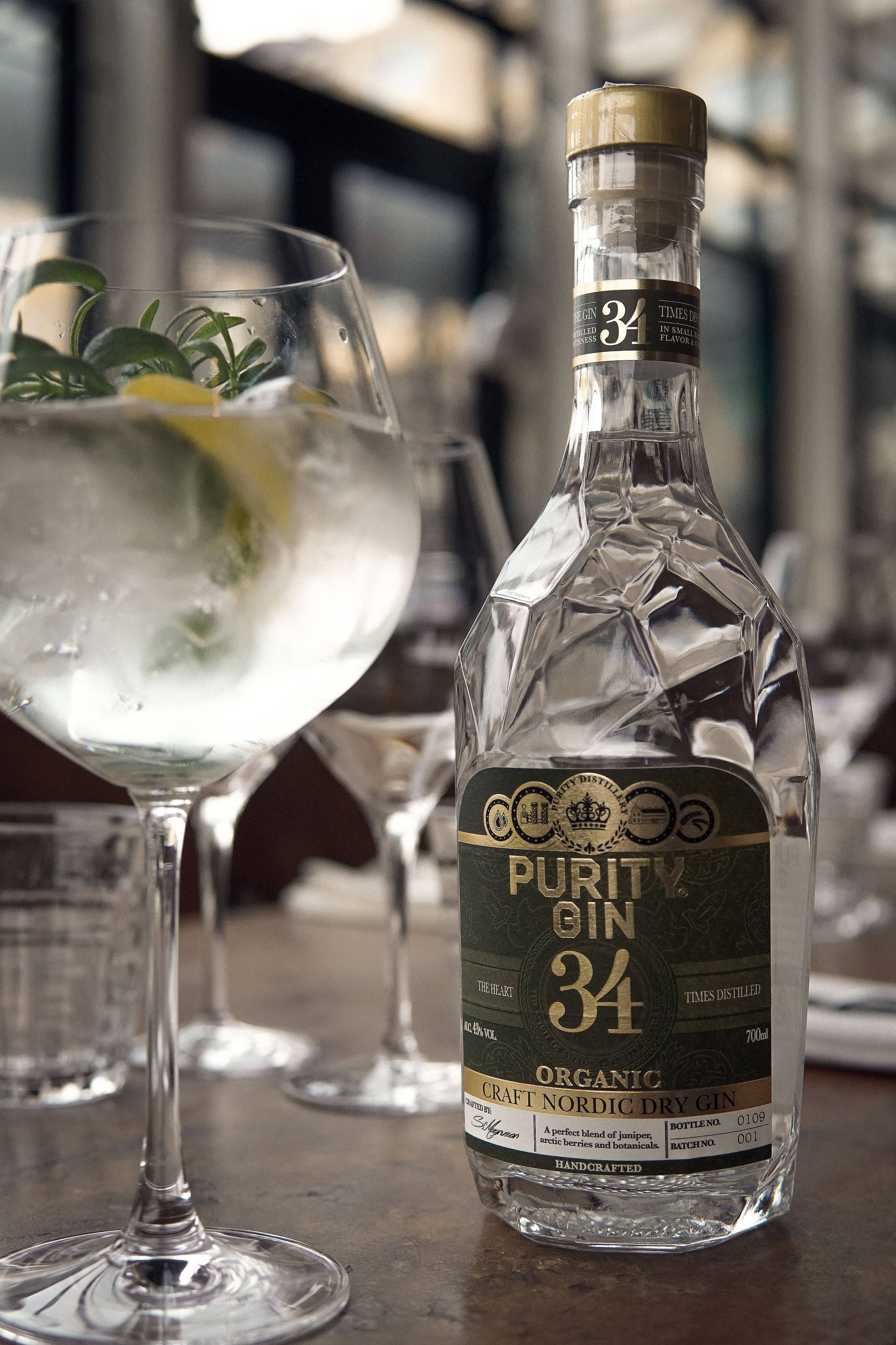 drinks 桌布 壁紙 — 一個透明的Purity Gin 34酒瓶放在木製吧檯上，旁邊是一杯以檸檬和香草裝飾的琴酒雞尾酒。