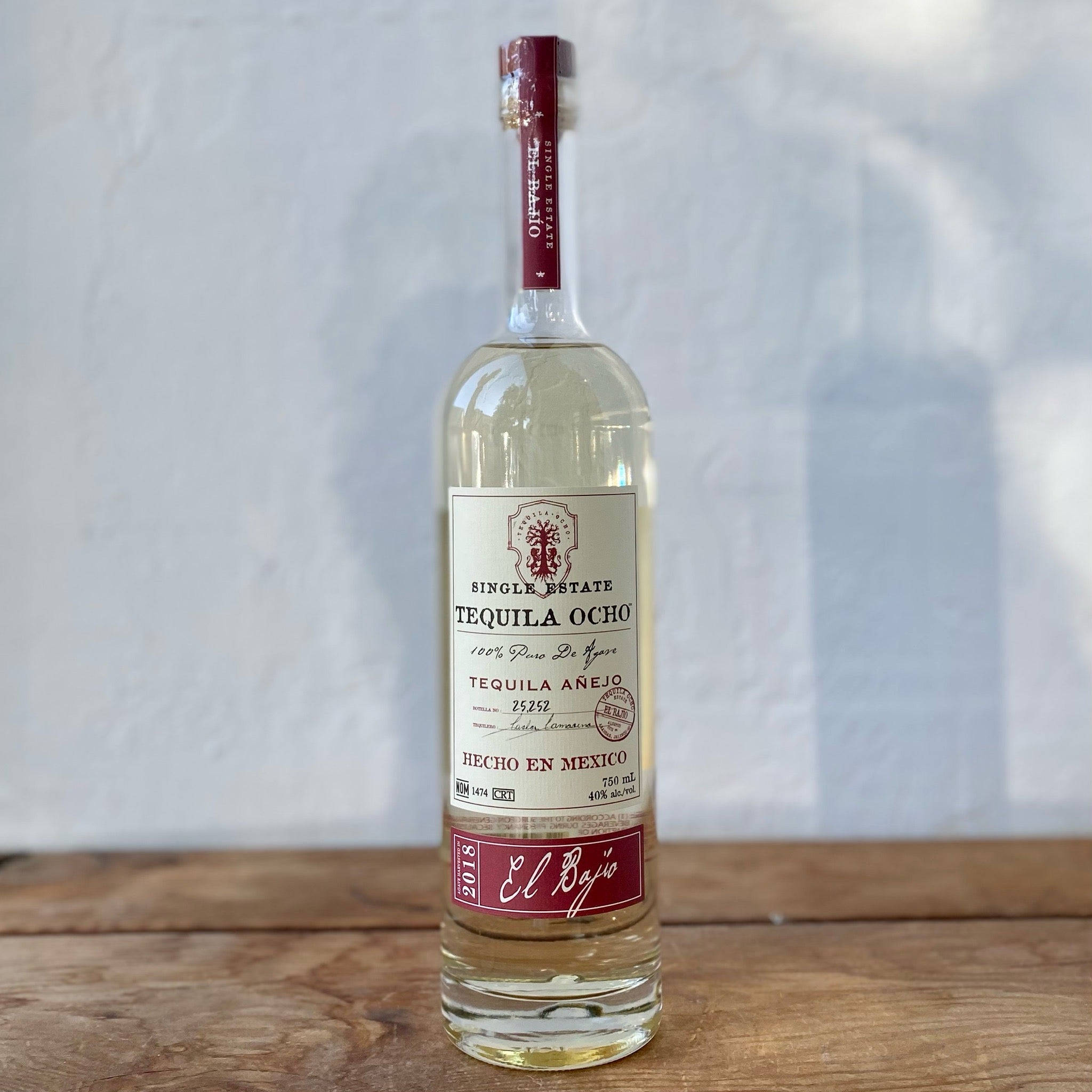 bottle 桌布 壁紙 — 一個透明的Tequila Ocho Añejo酒瓶放在質樸的木質表面上，背景是帶有紋理的白色牆壁。