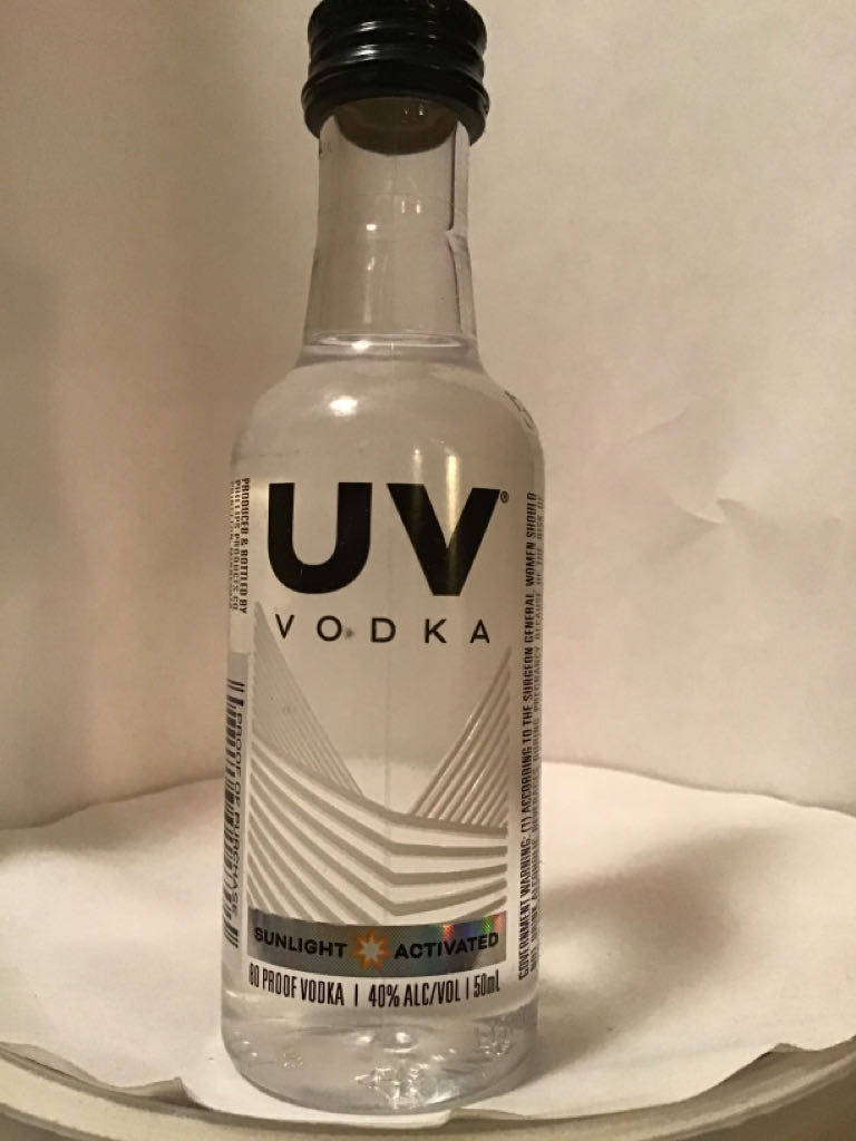 alcohol 桌布 壁紙 — 一個透明的UV伏特加酒瓶，黑色瓶蓋和幾何標籤，放在白色紙巾上，背景是純色的米白色。