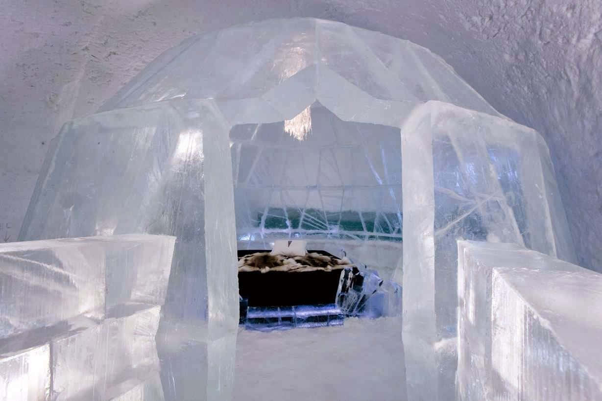 Ice Hotel 桌布 壁紙 — 一個透明的冰屋，裡面有一張毛皮襯裡的床，在雪白的室內柔和燈光下閃耀。