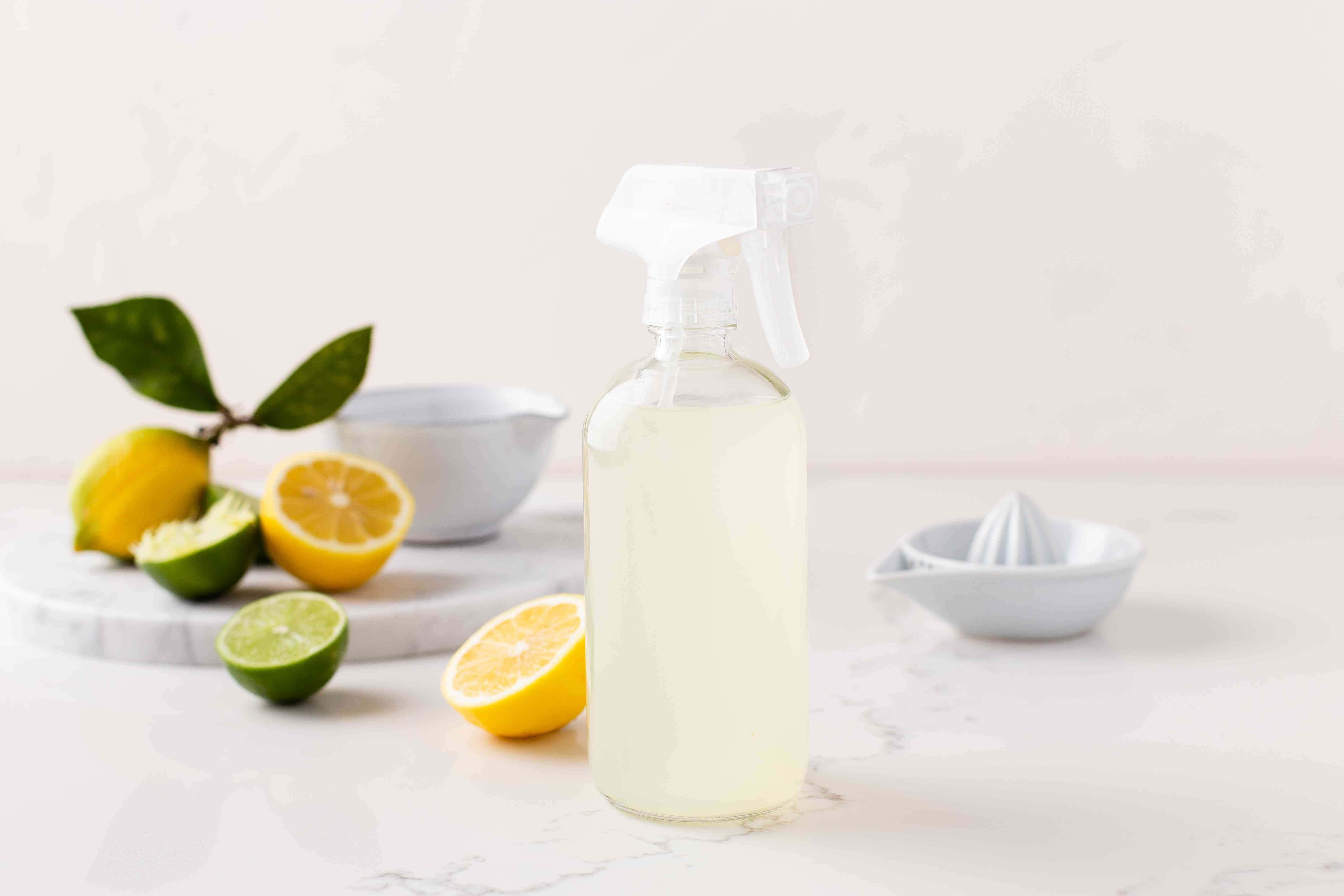 Lime 桌布 壁紙 — 一個透明的噴霧瓶裝滿檸檬萊姆清潔溶液，放在大理石檯面上，周圍是新鮮柑橘類水果和一個榨汁機。