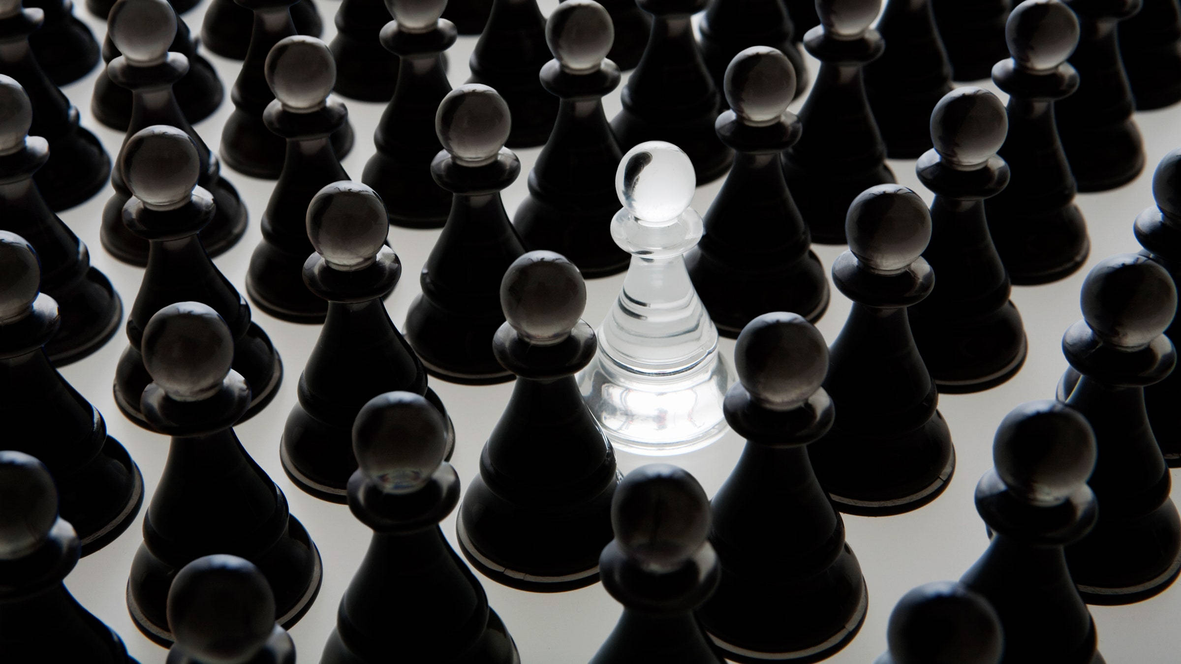 西洋棋 桌布 壁紙 — 一個透明的西洋棋兵在淺色表面上的一片黑色兵海中脫穎而出。