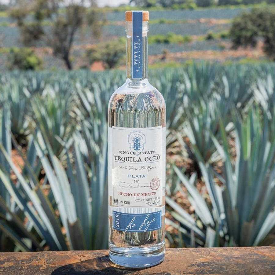 bottle 桌布 壁紙 — 一個透明的龍舌蘭酒瓶，標籤寫著 'Single Estate Tequila Ocho'，放在木質表面上，背景有龍舌蘭植物。