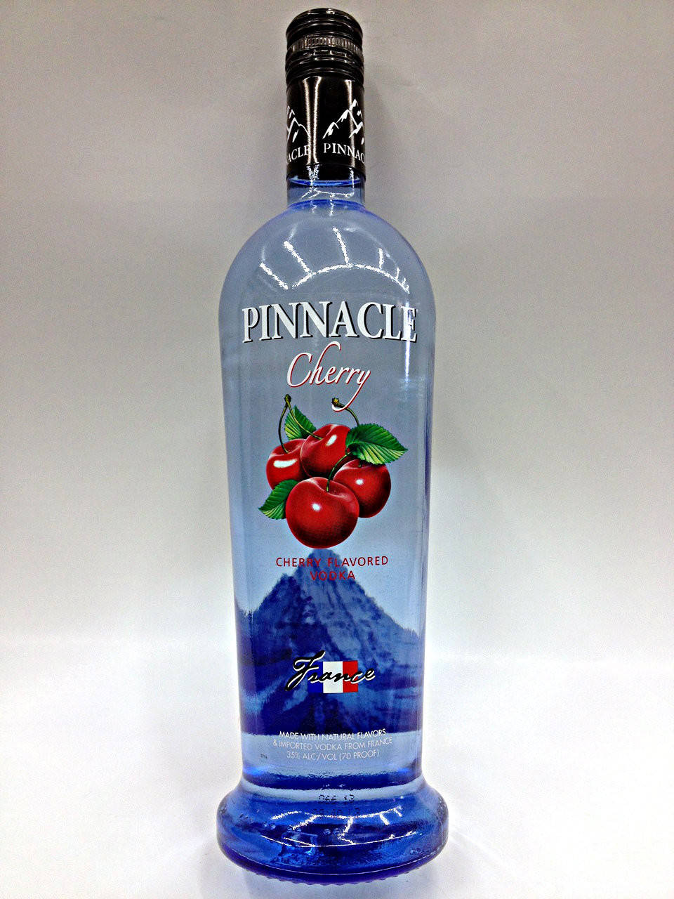 bottle 桌布 壁紙 — 一個透明藍色瓶子的Pinnacle Cherry伏特加，帶有紅色櫻桃和山脈圖案，背景為白色。
