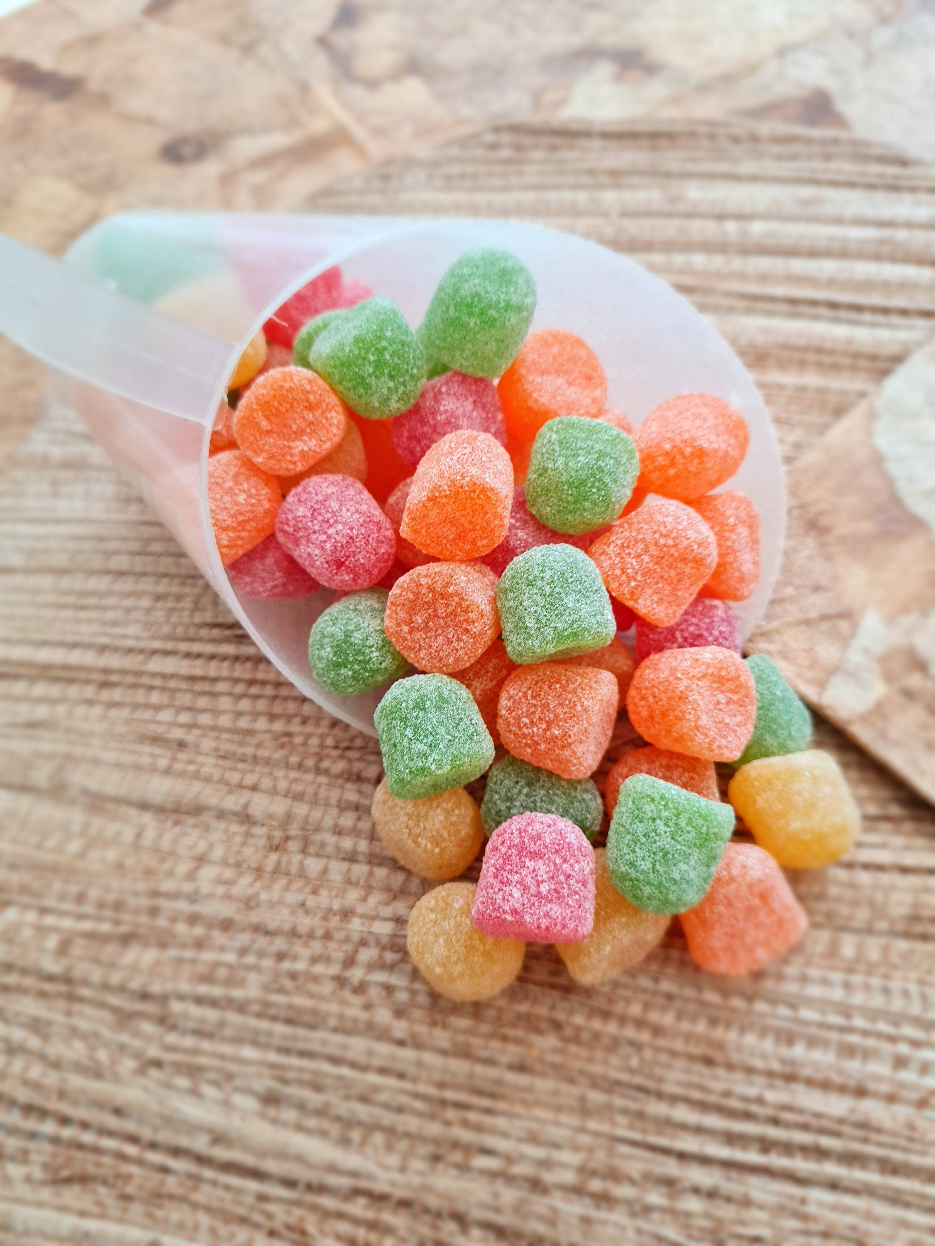 chewy 桌布 壁紙 — 一個透明錐體將鮮豔的橙色、粉紅色和綠色糖衣軟糖灑在紋理木質表面上。