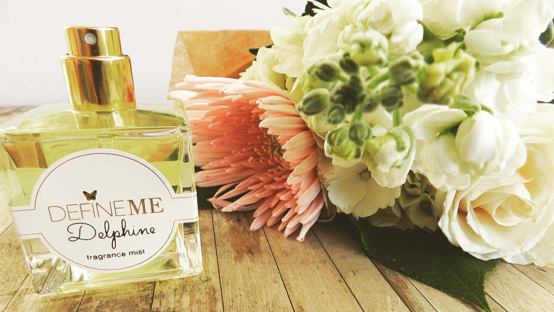 Floral Fragrance 桌布 壁紙 — 一個透明香水瓶配金色瓶蓋，放在木質表面上，旁邊是一束白玫瑰和粉紅色非洲菊雛菊。