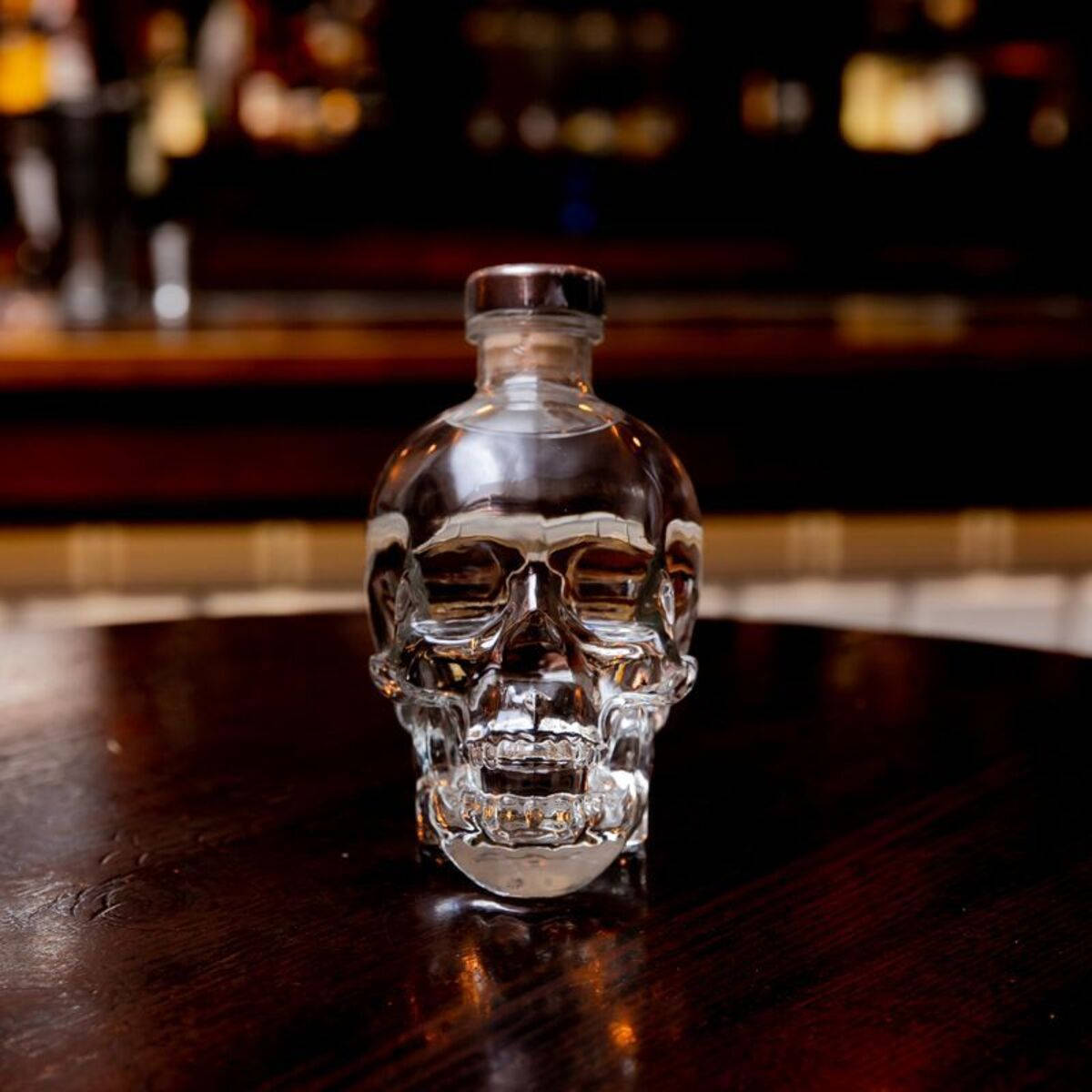 Drink 桌布 壁紙 — 一個透明骷髏形狀的伏特加酒瓶放在深色木吧檯上，背景有模糊的溫暖燈光。